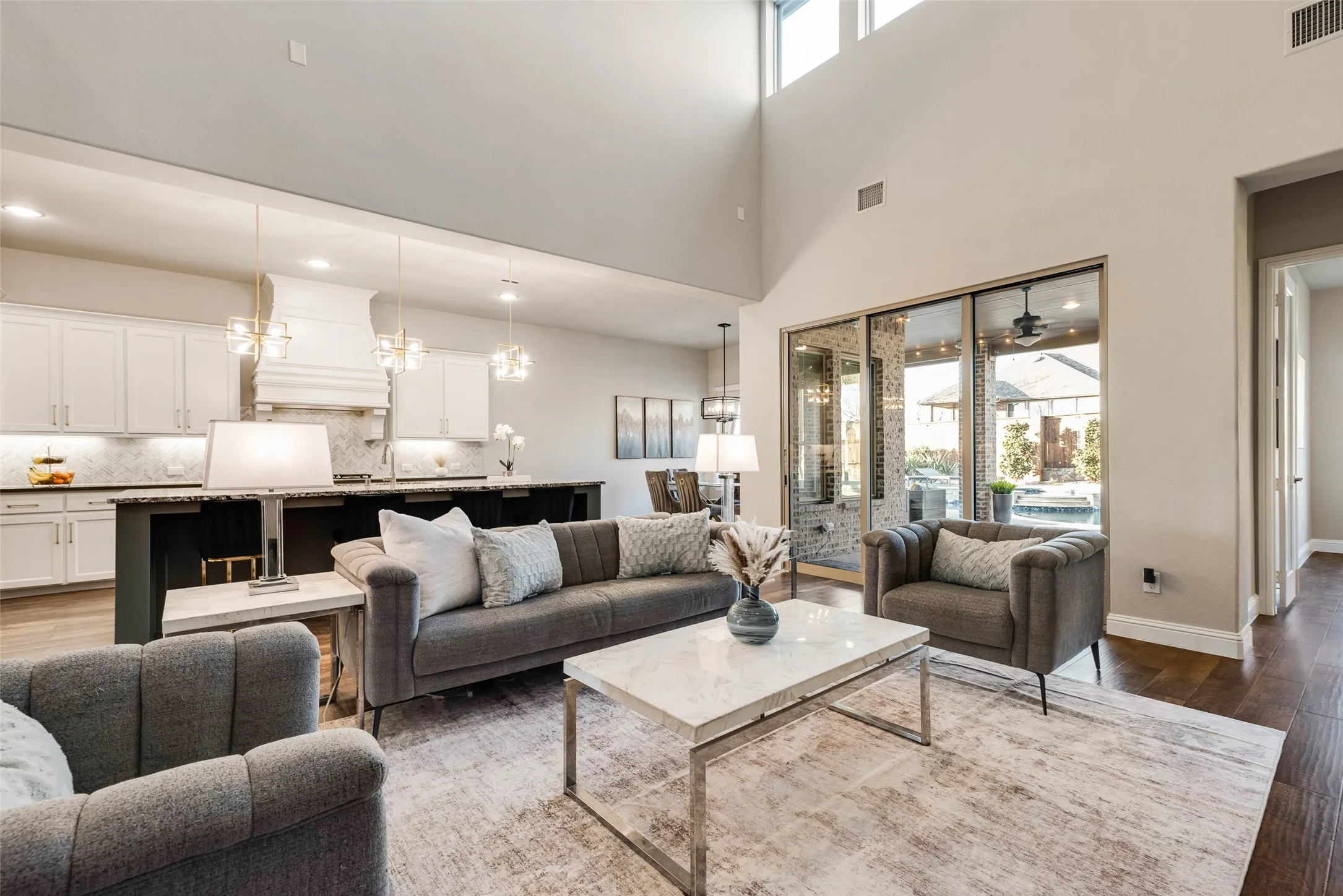 Open-concept living space featuring high ceilings with upper windows, wood-finish flooring, and a contemporary kitchen with white cabinetry and pendant lighting