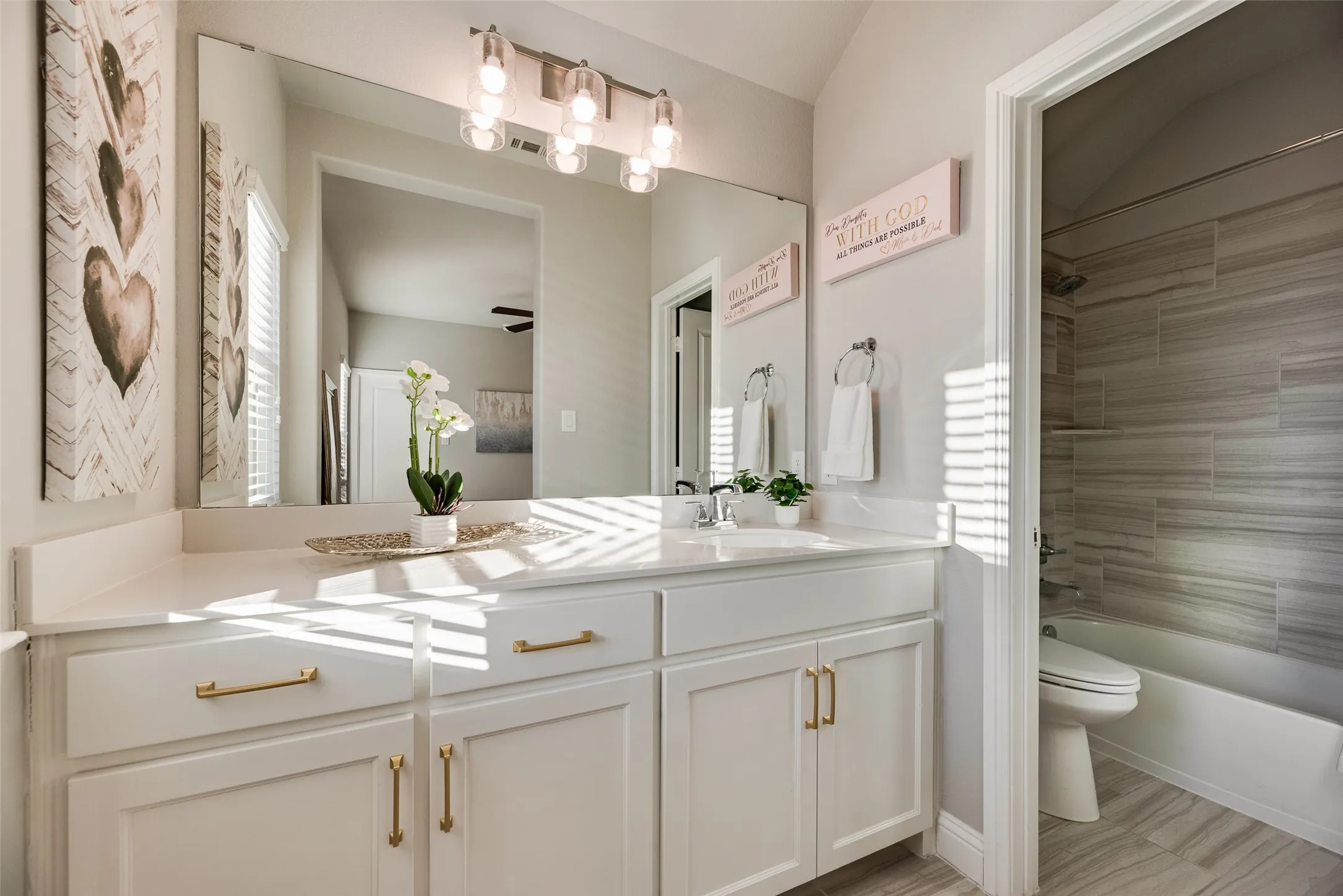 Bathroom vanity featuring a single basin, white countertop, white cabinetry with gold-toned hardware, and a large wall-mounted mirror
