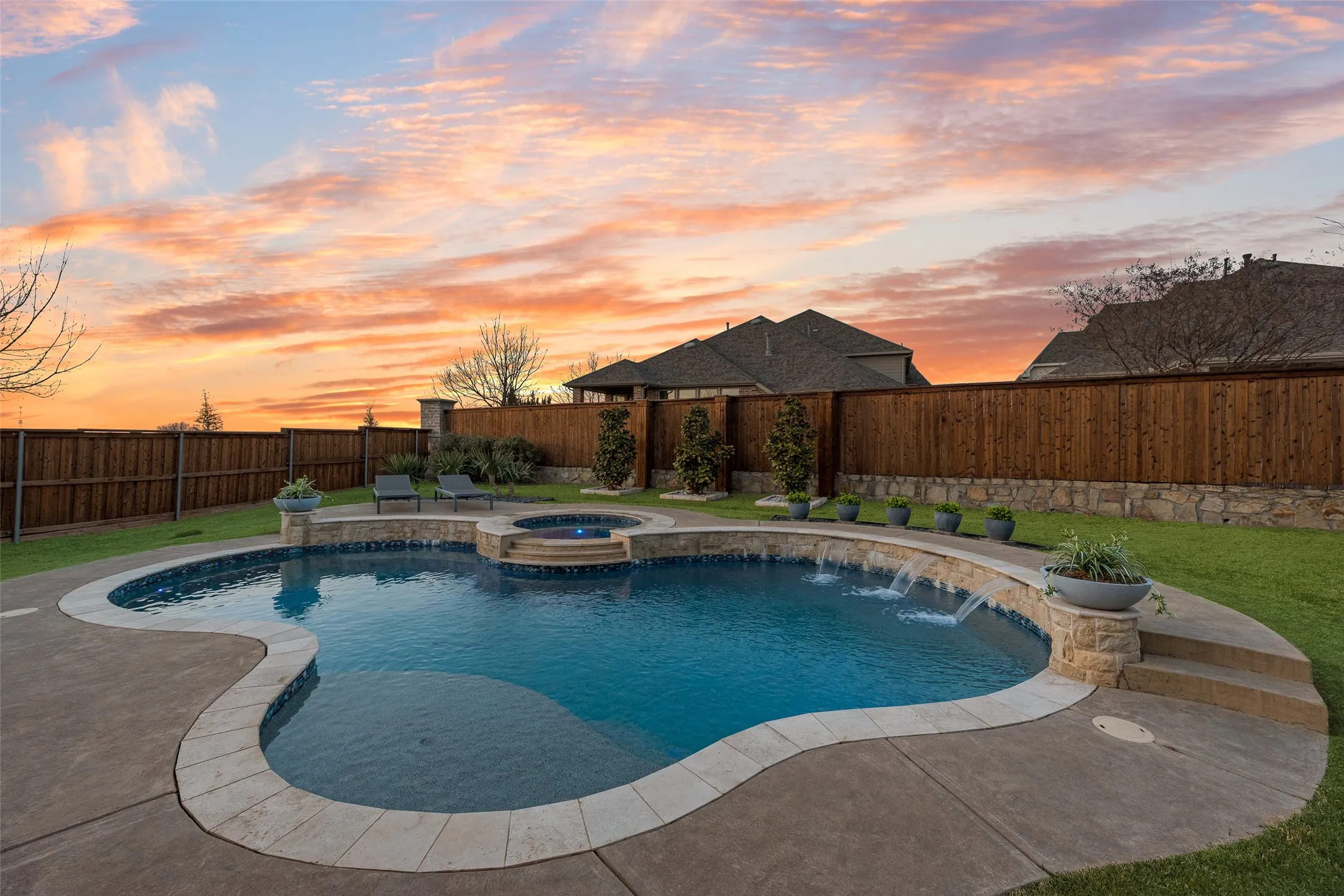 Freeform swimming pool with integrated spa and water features, surrounded by a concrete patio and manicured lawn