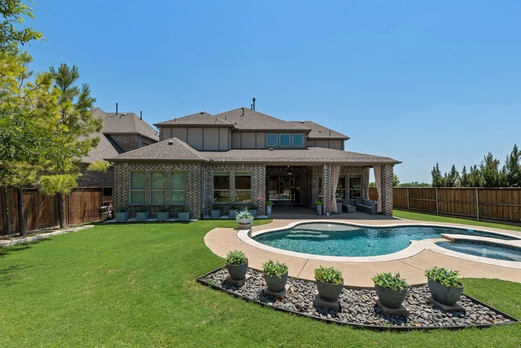 Expansive backyard featuring a custom-shaped swimming pool with an integrated spa, extensive concrete decking, and a covered patio area