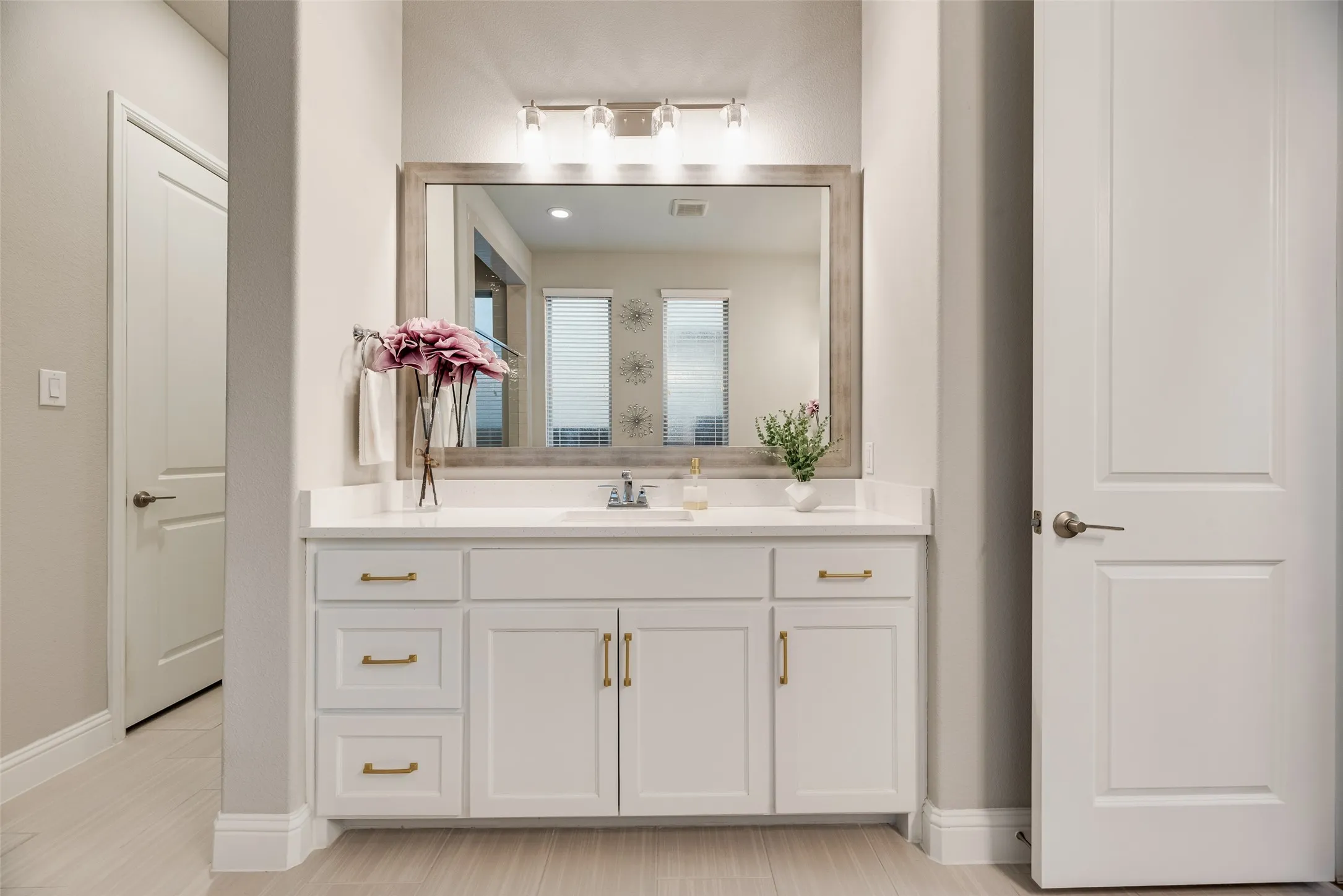 Bathroom vanity featuring a white countertop, under-mount sink, and brass hardware on white cabinetry