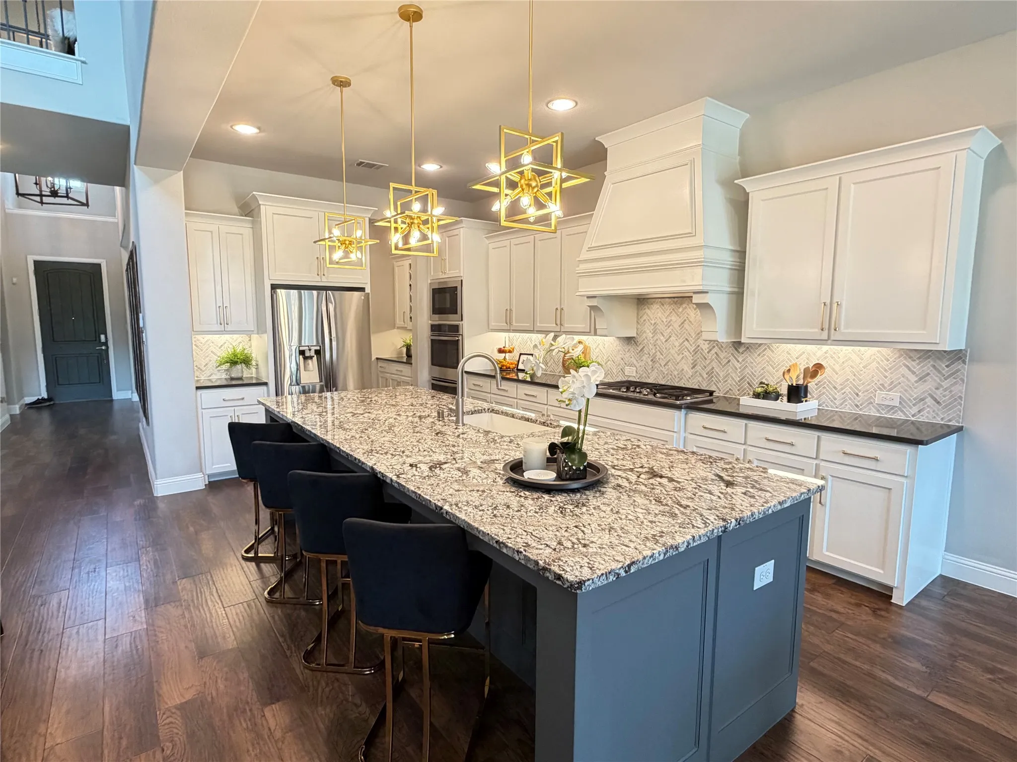 Gourmet kitchen featuring a large island with a speckled countertop, white cabinetry, herringbone tile backsplash, wood-finish flooring, and stainless steel appliances