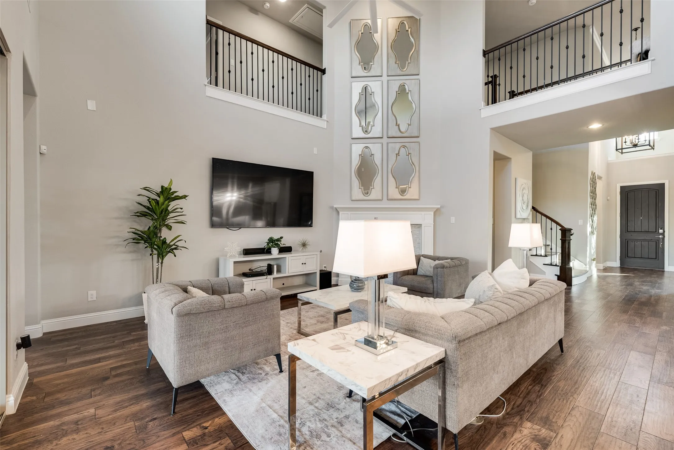 Two-story living area featuring wood-finish flooring, a white mantel, and an upper-level balcony with black iron railings