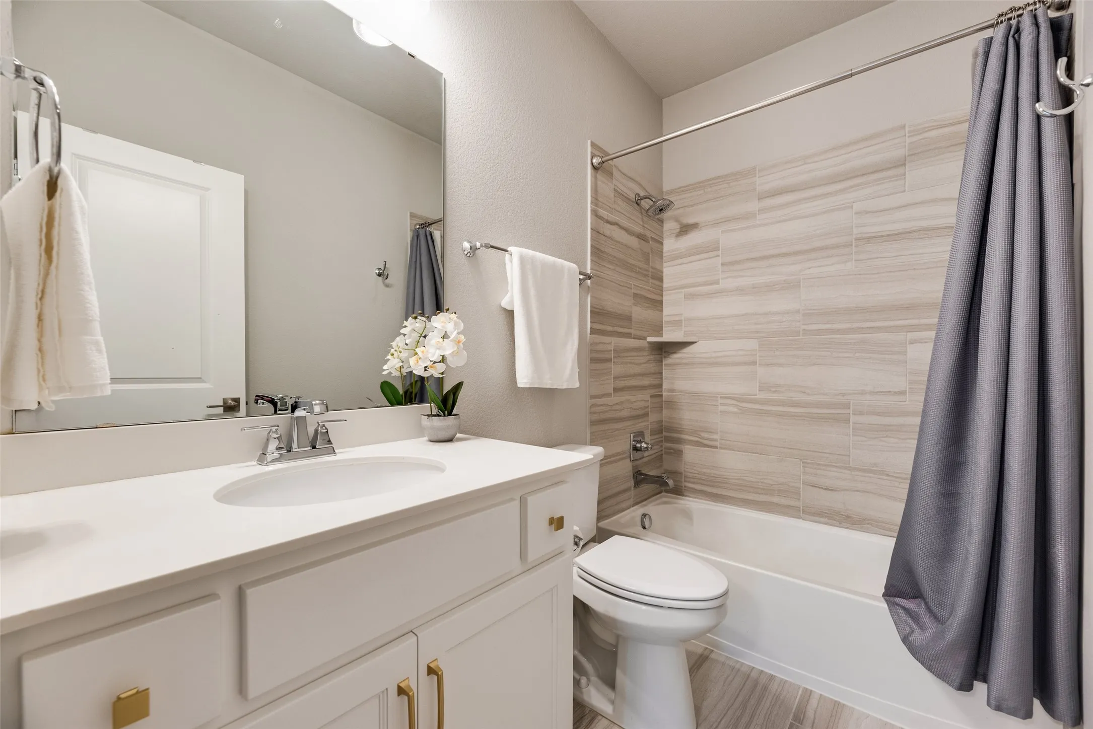 Full bathroom featuring a white vanity with gold-finish hardware, a single undermount sink, and a large mirror