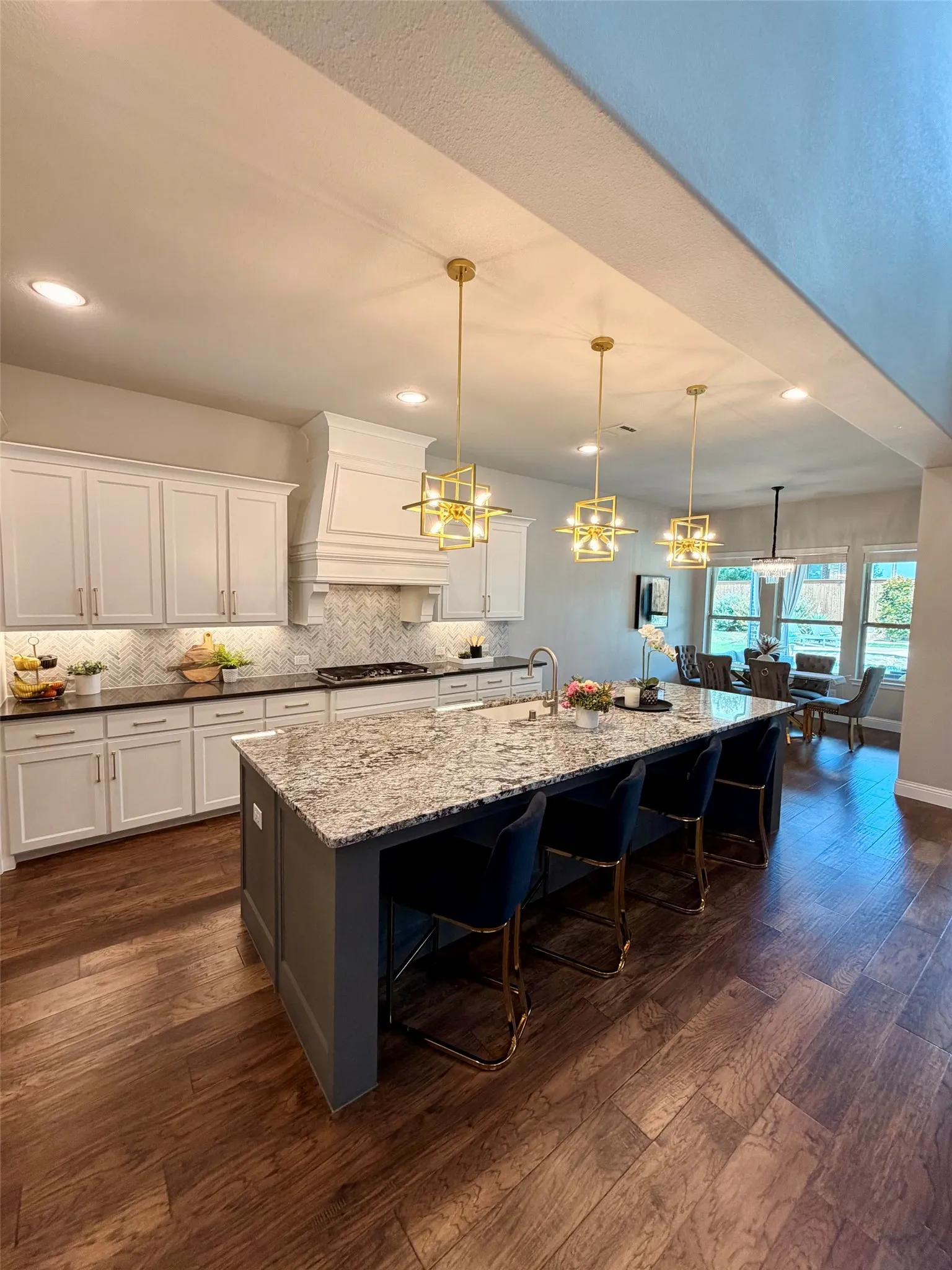 Gourmet kitchen featuring a large island with seating, stone countertops, white cabinetry, a decorative range hood, and wood-finish flooring