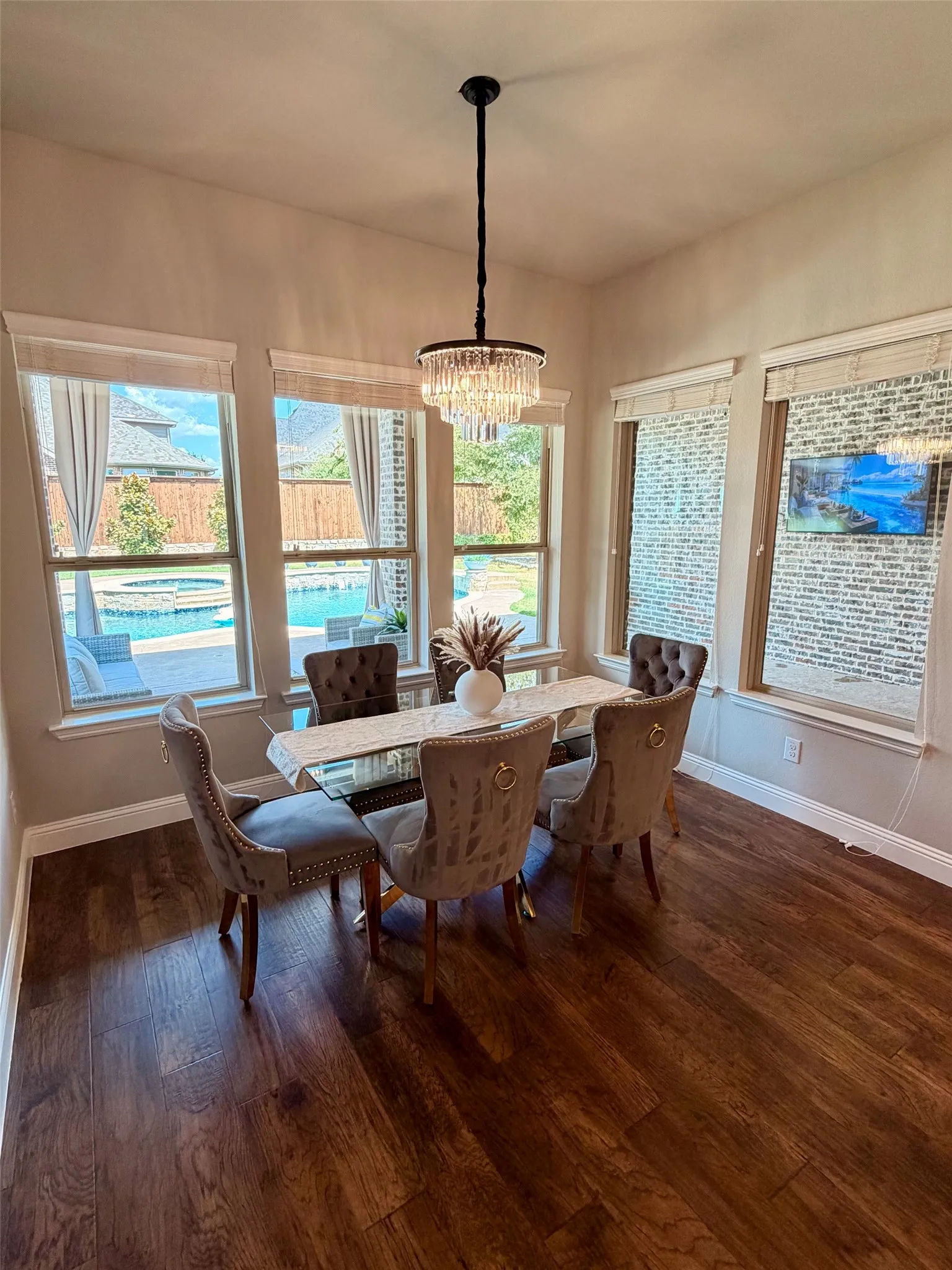 Wood-finish flooring, multiple windows, crystal chandelier, and a pool visible through the windows