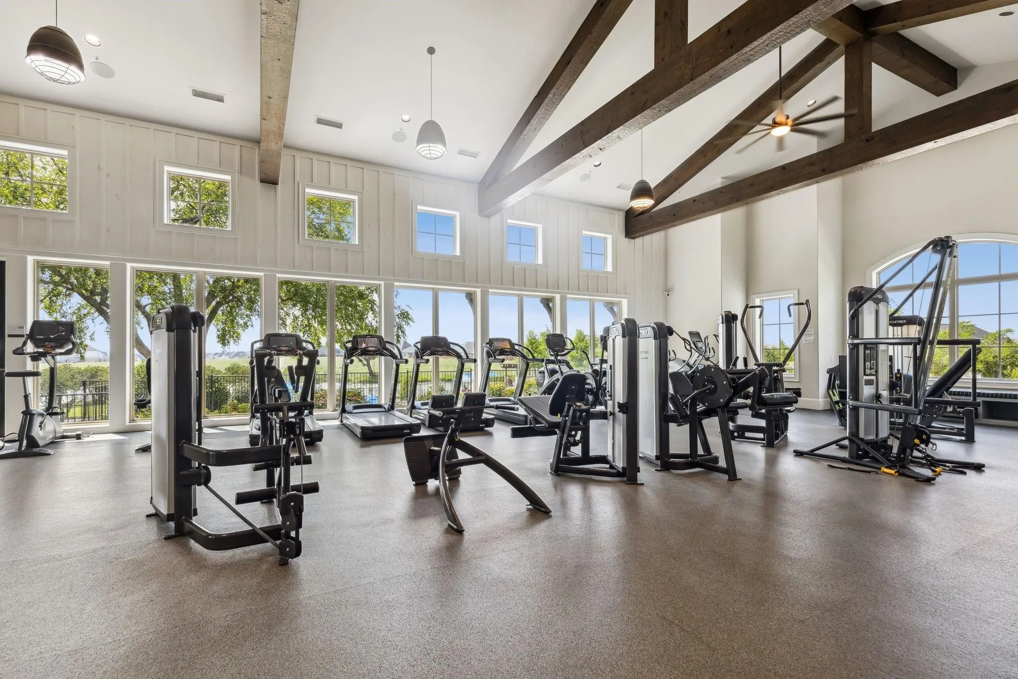CLLUB HOUSE GYM - Spacious fitness area featuring extensive gym equipment, high vaulted ceilings with exposed wood beams, and a wall of large windows overlooking exterior scenery