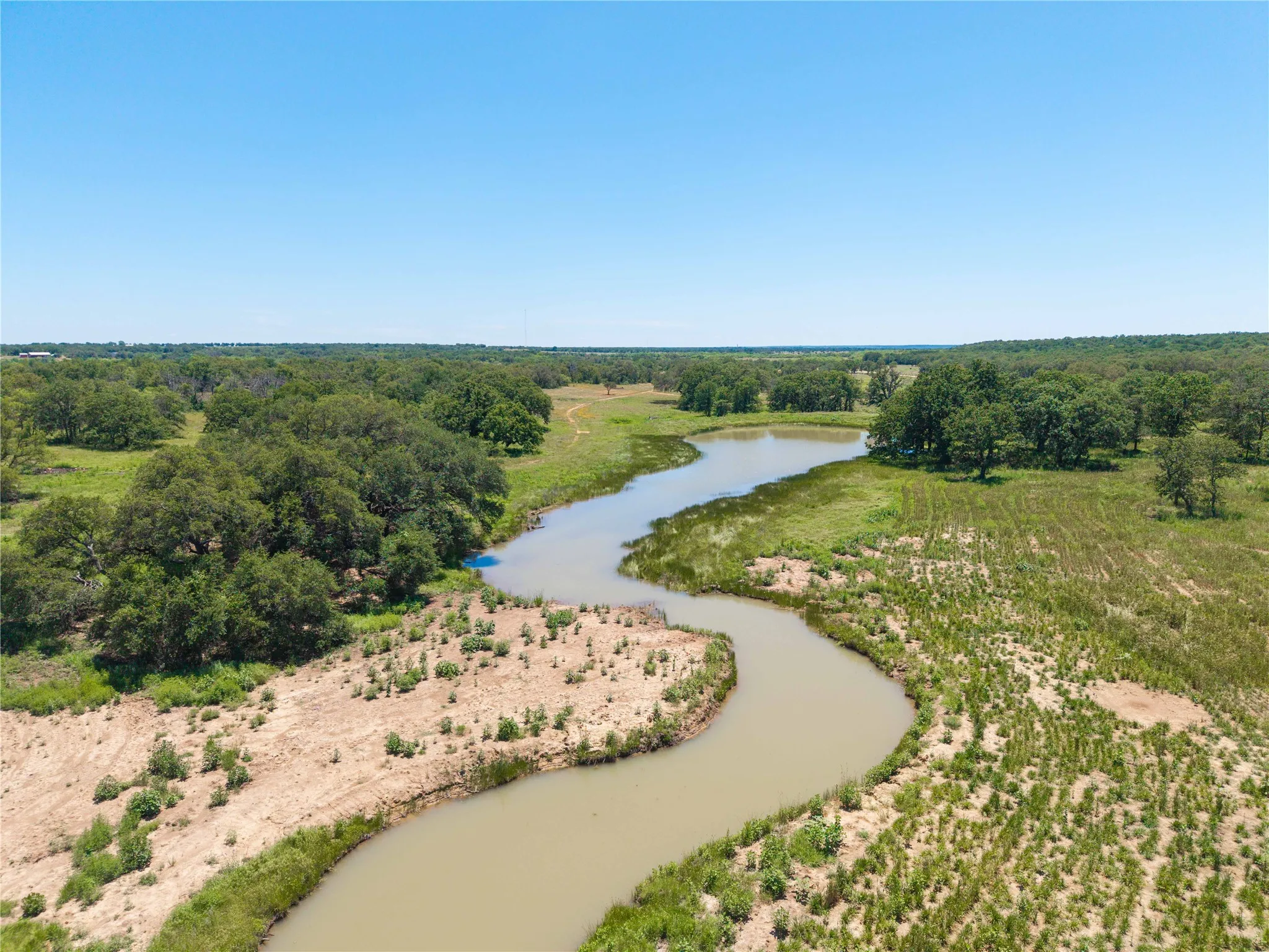 Expansive natural landscape featuring a winding waterway, mature trees, and varied terrain