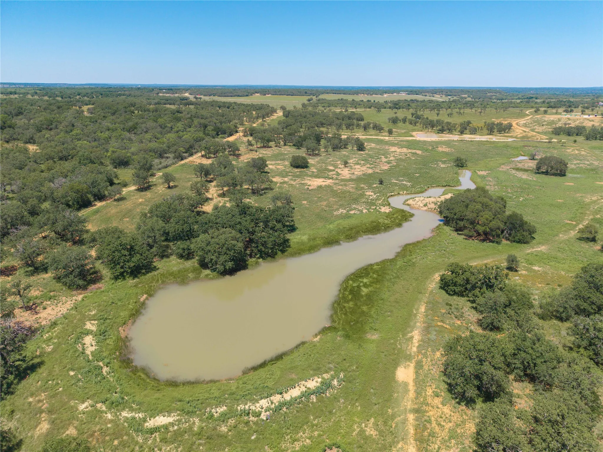 Expansive rural landscape featuring a large pond and winding creek