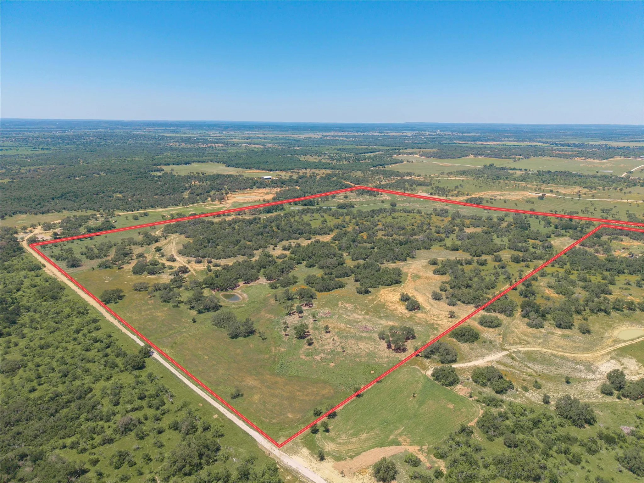 Expansive rural property featuring varied topography, a tranquil pond, scattered mature trees, and a clear boundary line
