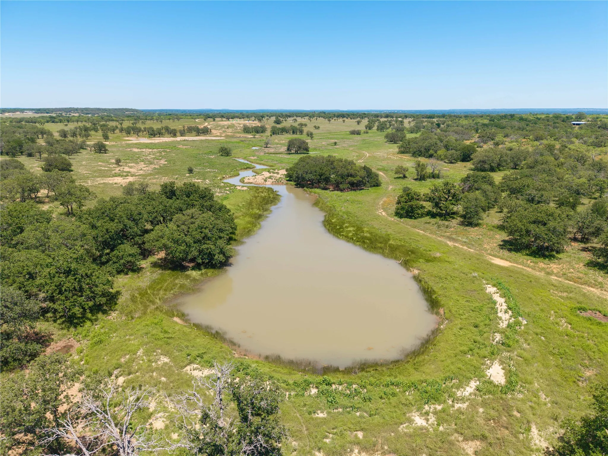 Expansive rural landscape featuring a large pond, mature trees, and natural grassland