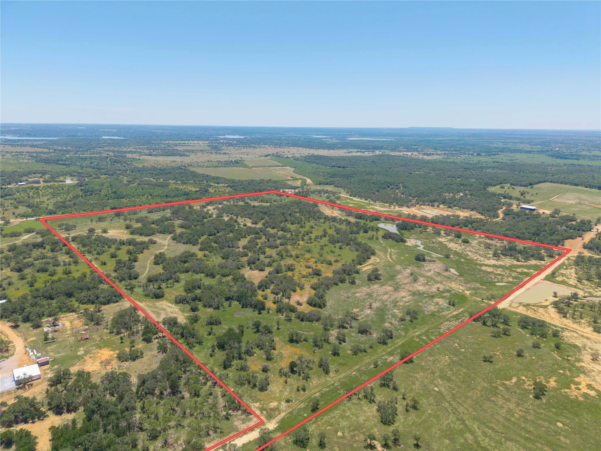 Expansive rural acreage featuring scattered trees, open clearings, natural water features, and a distant horizon
