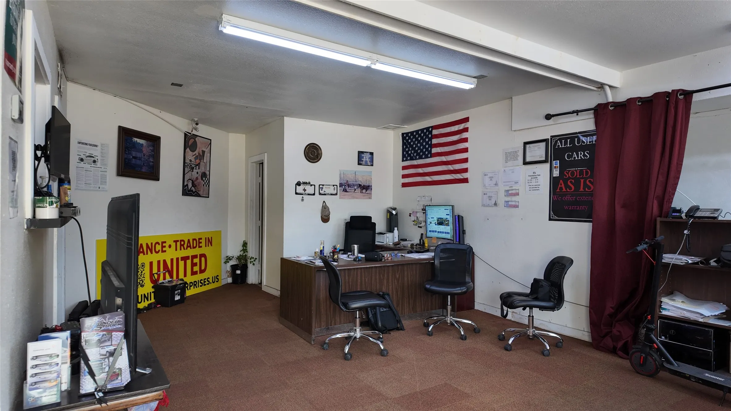 Commercial interior space featuring an office desk, brown carpet, white walls, and fluorescent lighting