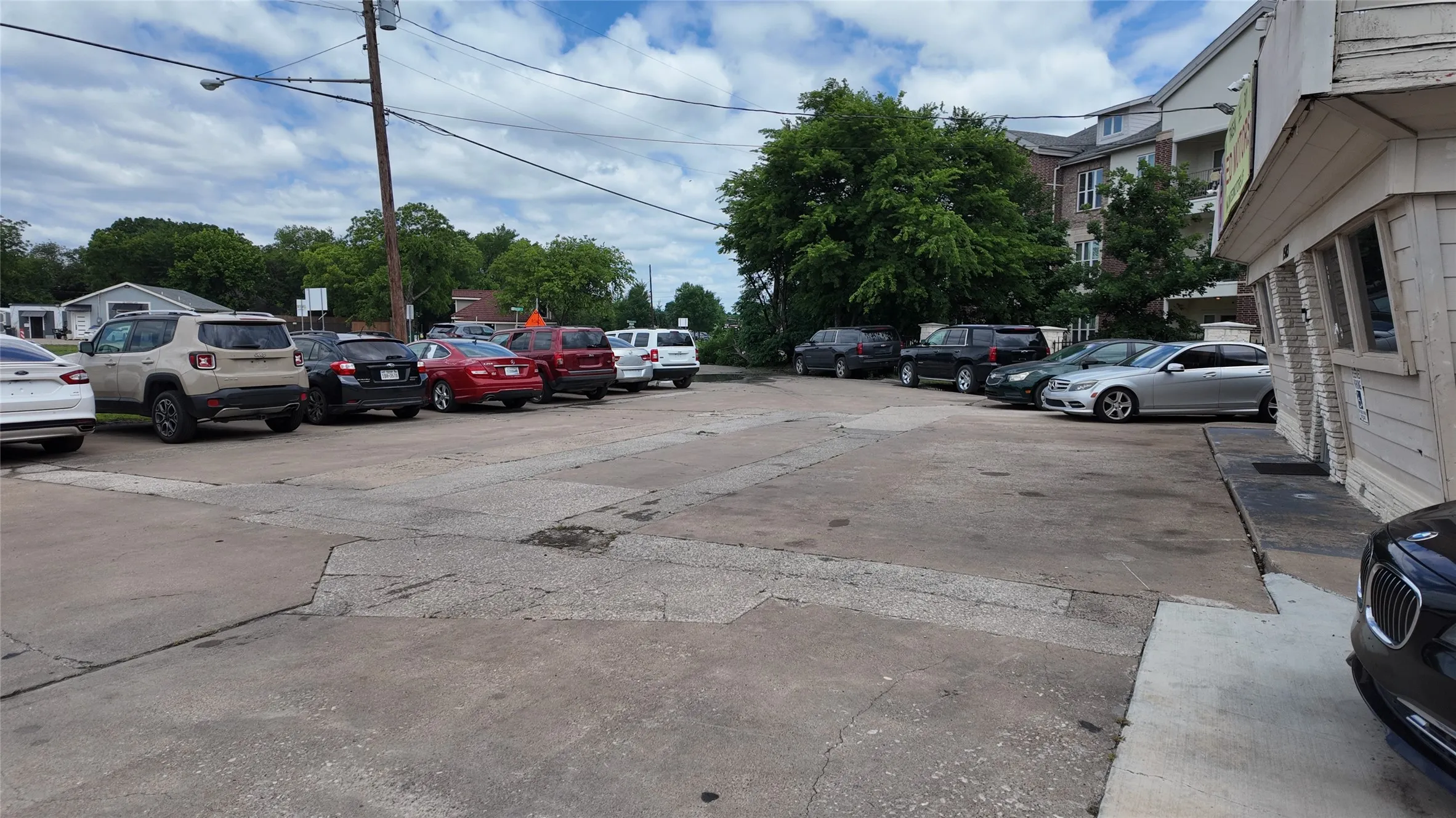 Paved parking area with multiple parking spaces, bordered by a building with horizontal siding and visible windows