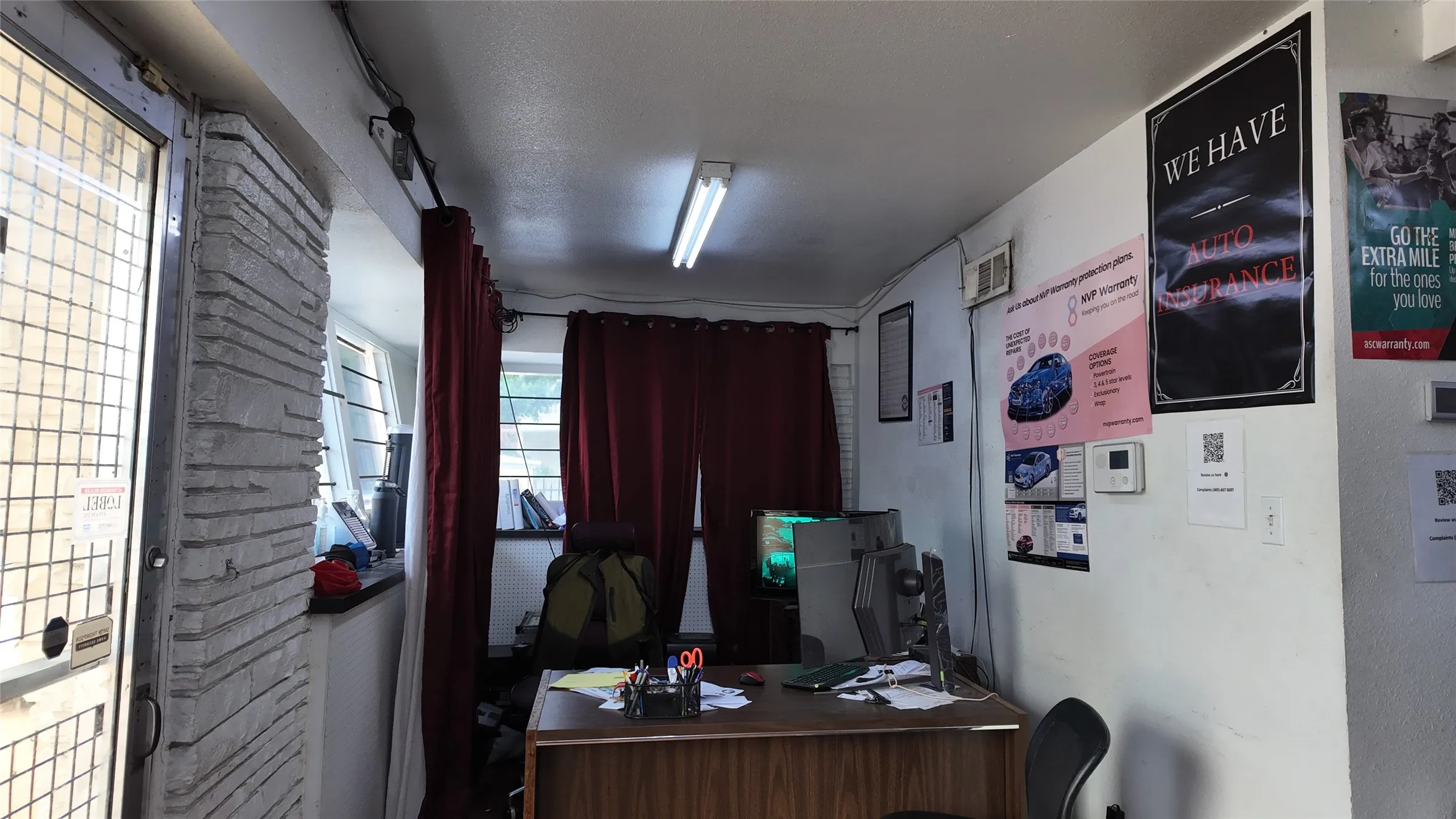 Interior commercial space featuring a wood-finish desk, fluorescent ceiling lighting, and a window with red drapery