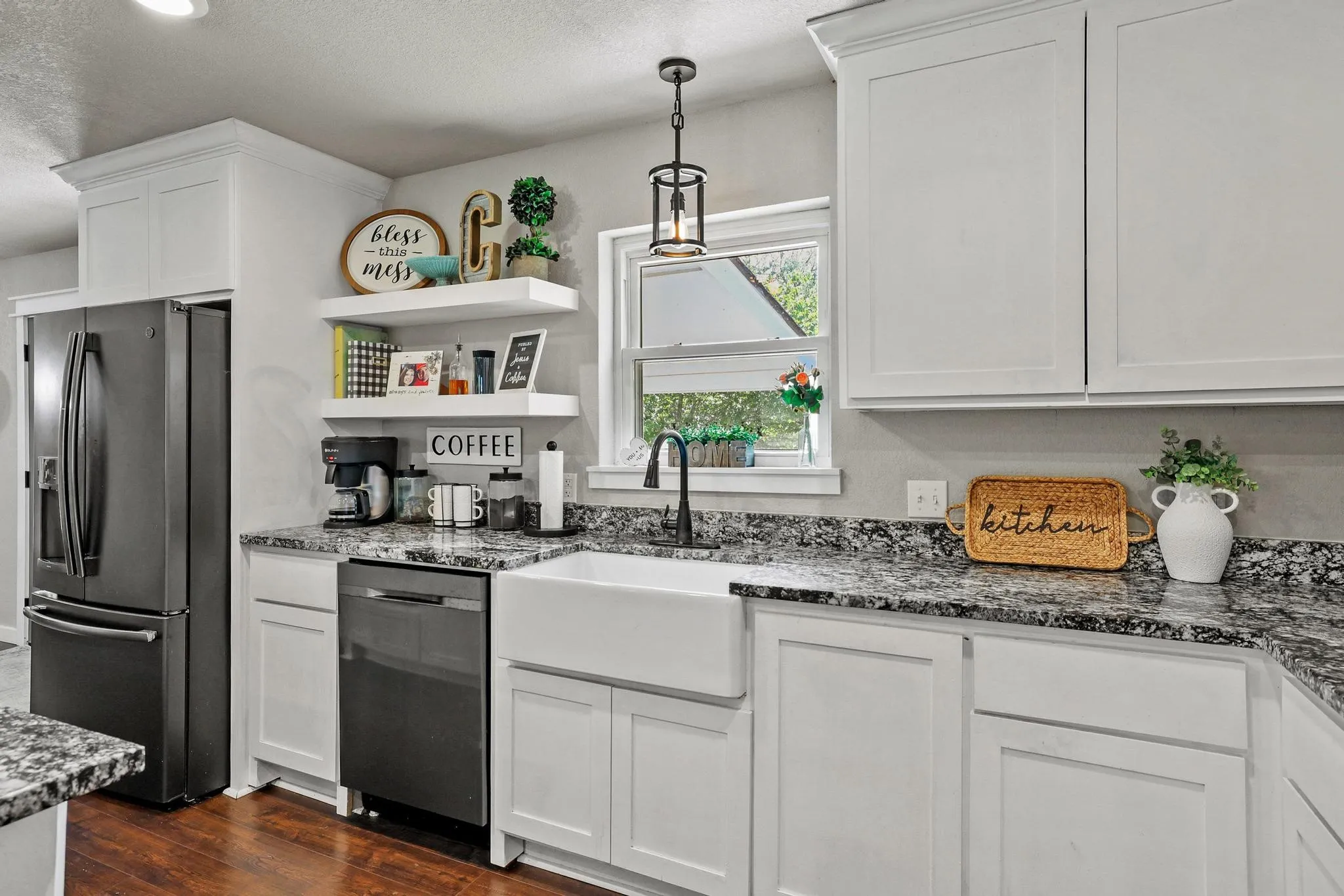 Modern kitchen featuring white shaker cabinetry, speckled countertops, a farmhouse sink with a matte black faucet, and wood-finish flooring