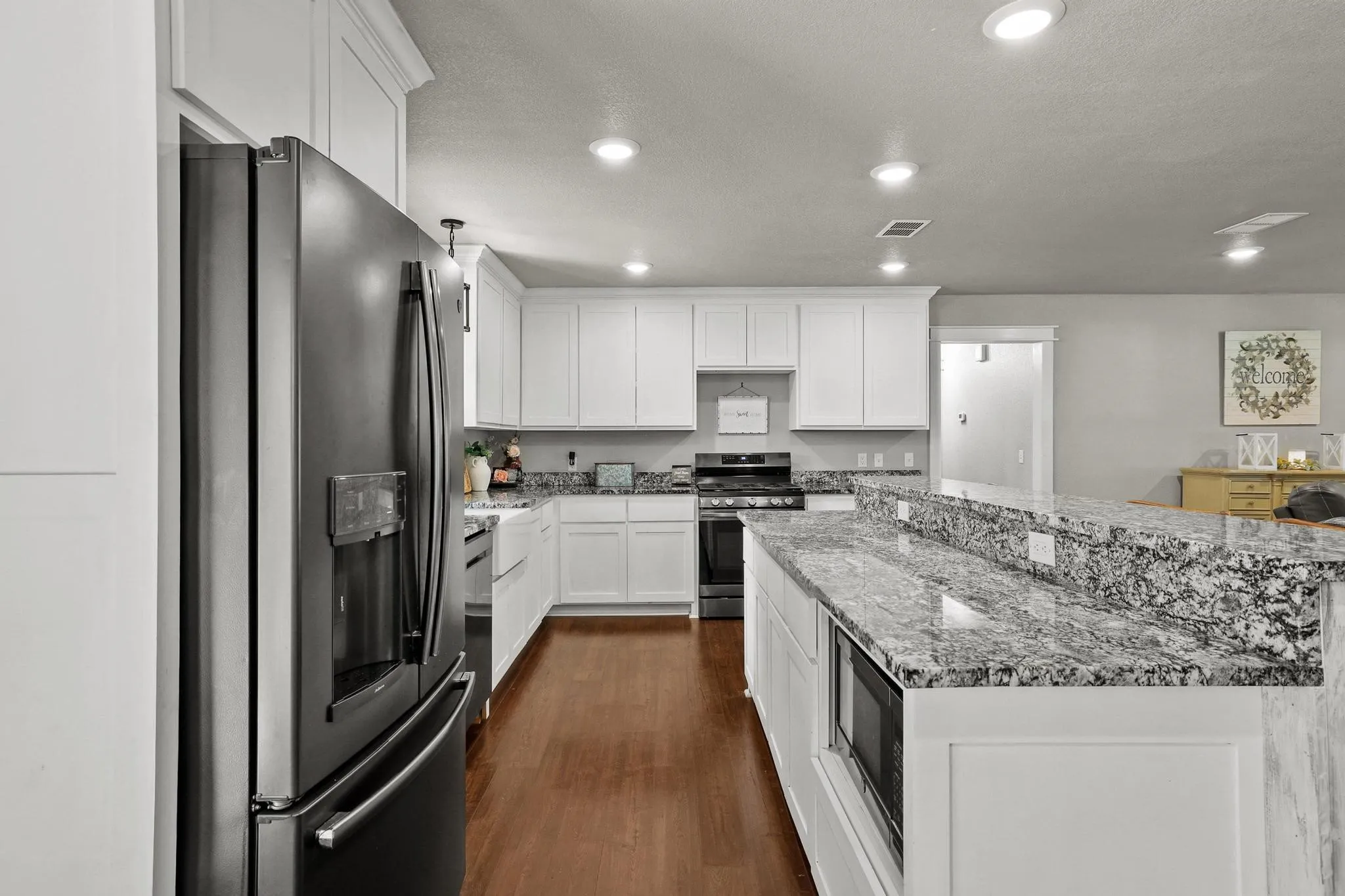 Contemporary kitchen featuring white cabinetry with crown molding, dark wood-finish flooring, recessed lighting, and speckled countertops