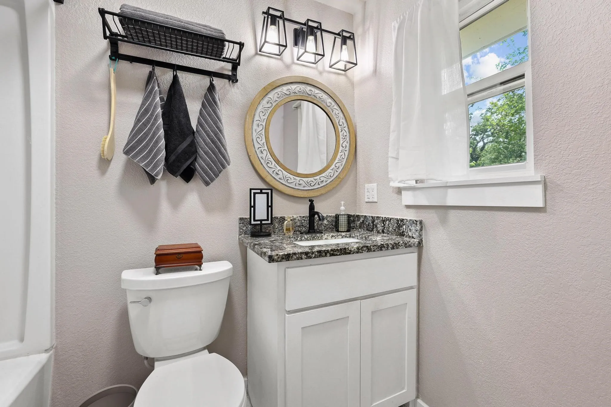 Bathroom featuring a white vanity with a granite-style countertop, a circular mirror with an ornate frame, and a three-light fixture with black metal cages