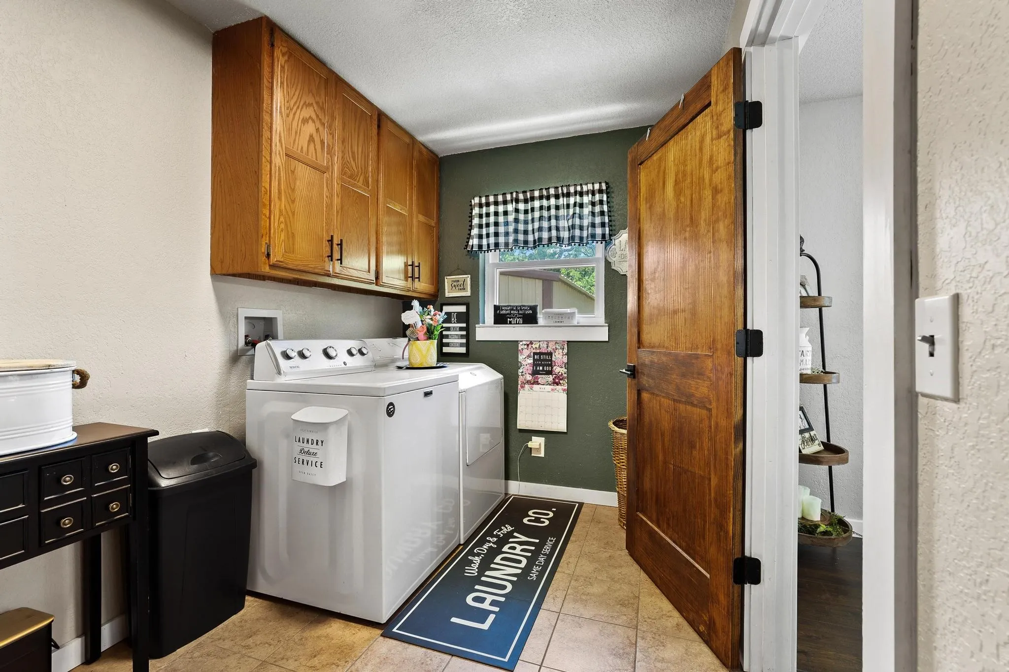 Dedicated laundry space featuring wood cabinetry, a window with a checkered valance, and tile flooring