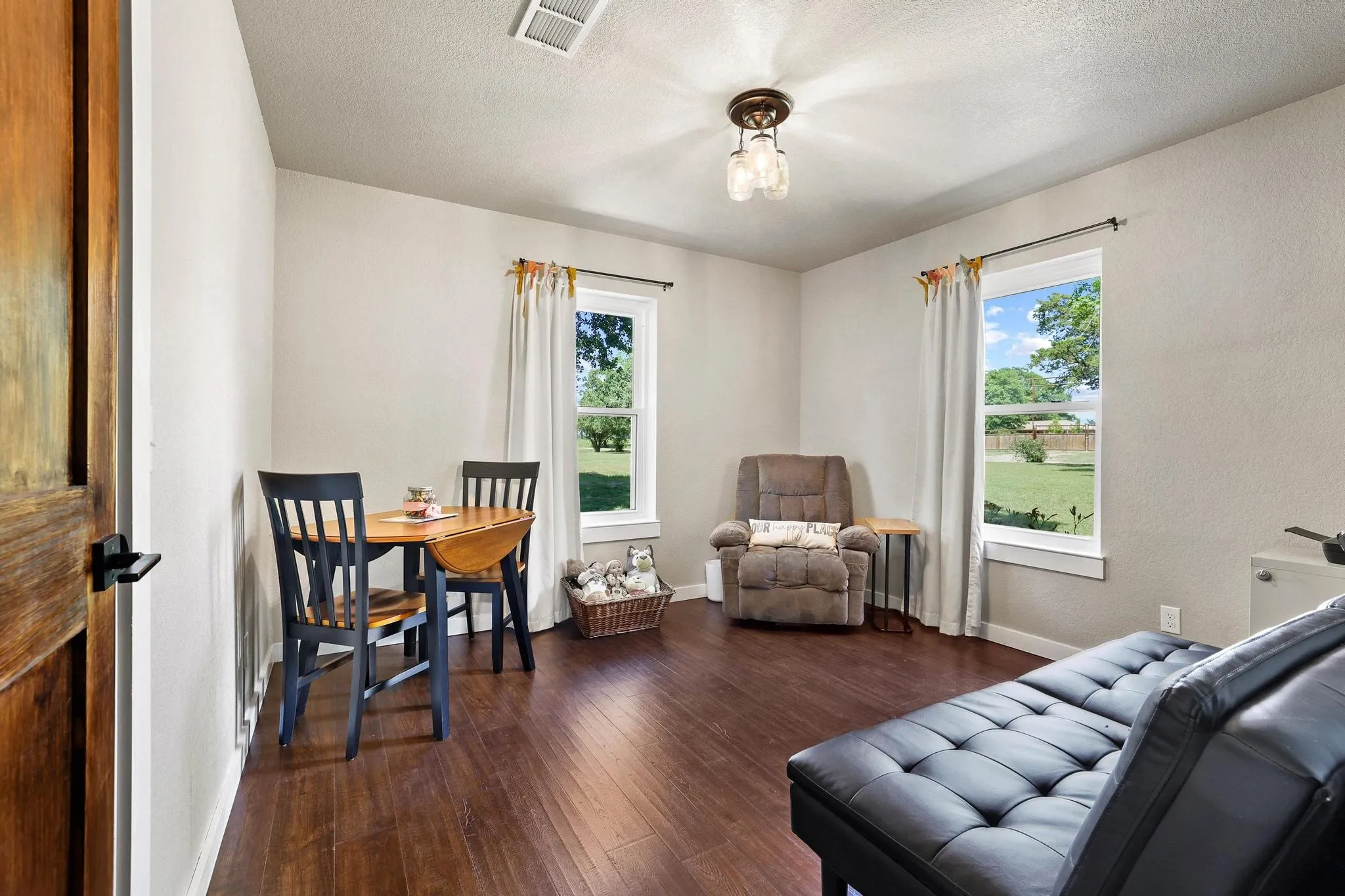 Spacious room featuring rich wood-finish flooring, light-toned walls, and a multi-bulb ceiling fixture