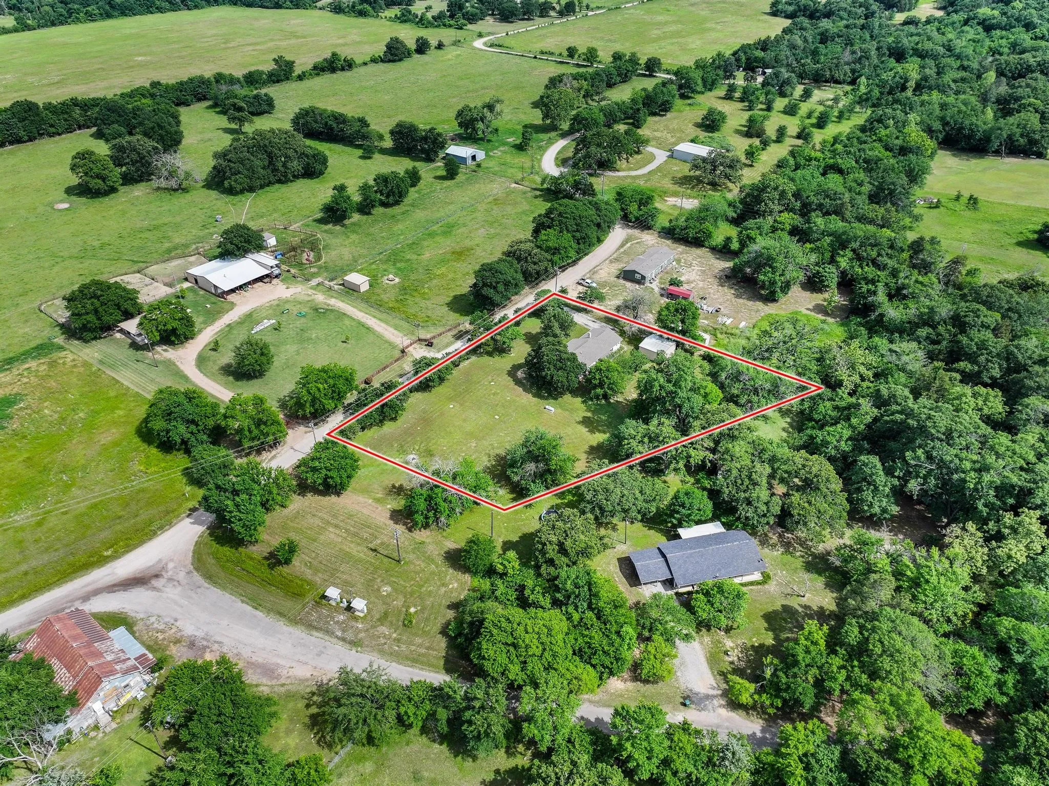 Expansive rural property featuring a primary residence with an attached garage, surrounded by mature trees and open green spaces