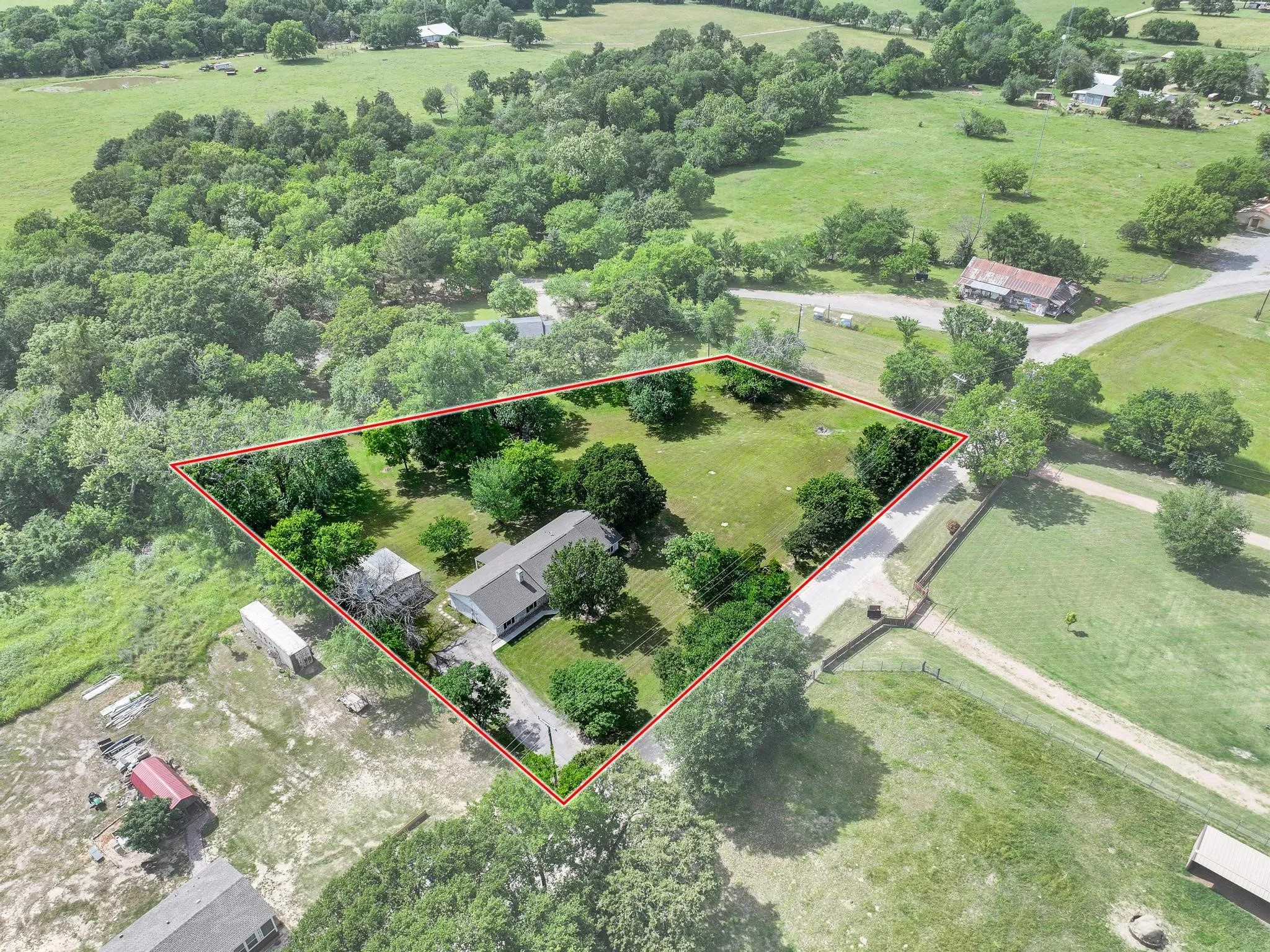Expansive property featuring a main residence, a secondary structure, mature trees, and a gravel driveway
