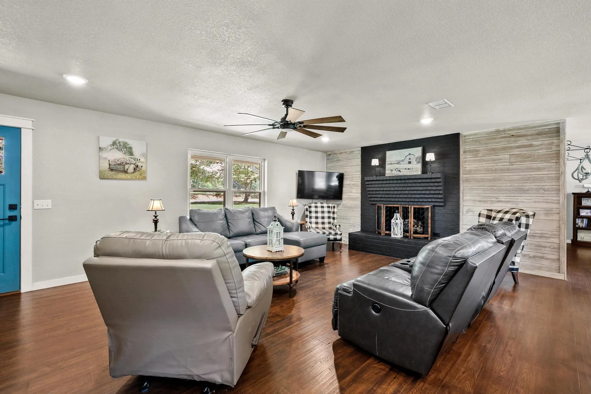 Living area featuring rich wood-finish flooring, a prominent black brick fireplace, and accent shiplap wall paneling