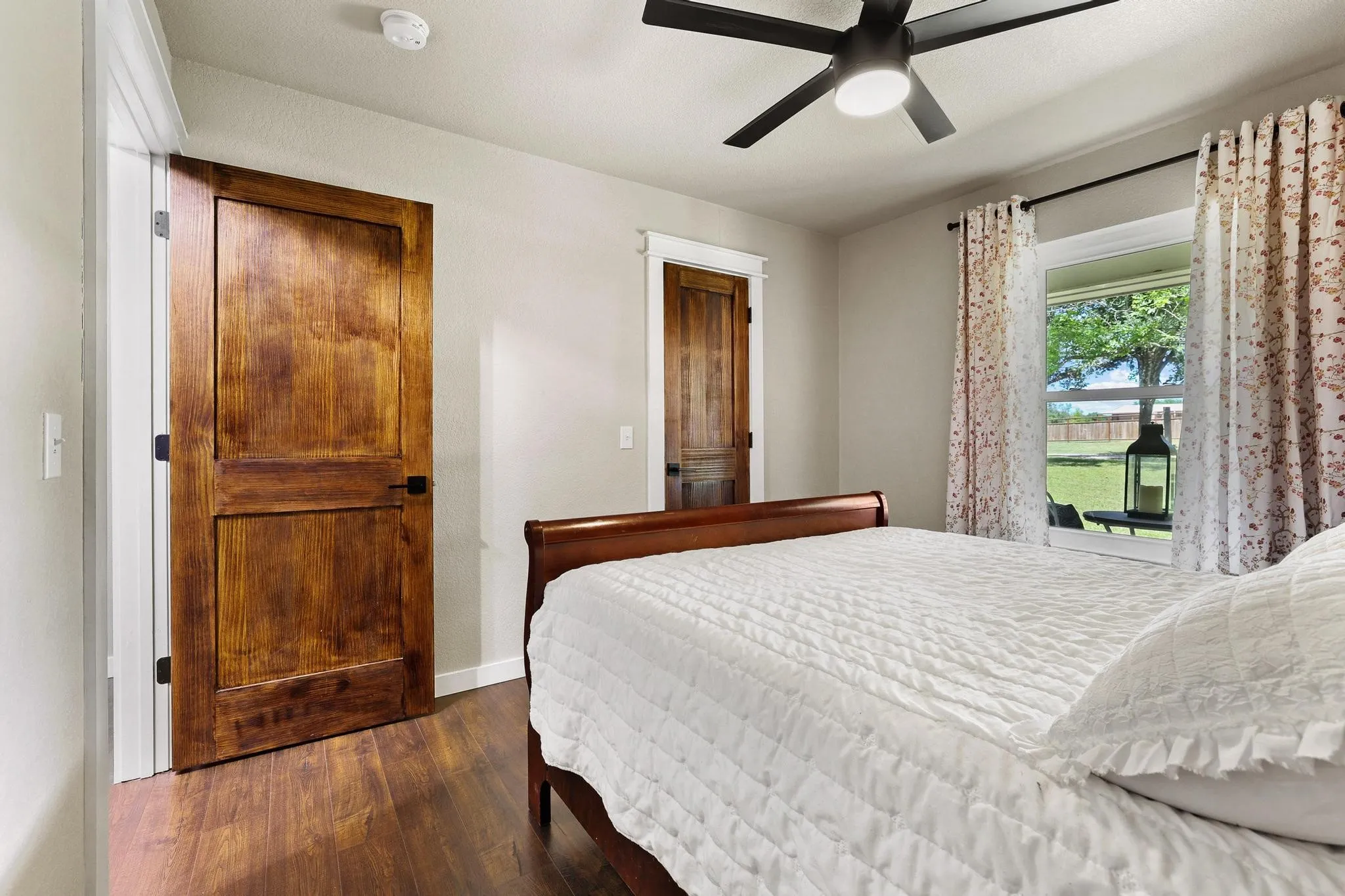 Bedroom featuring wood-finish flooring, a ceiling fan with integrated lighting, two panel-style wood doors, and a window with white trim