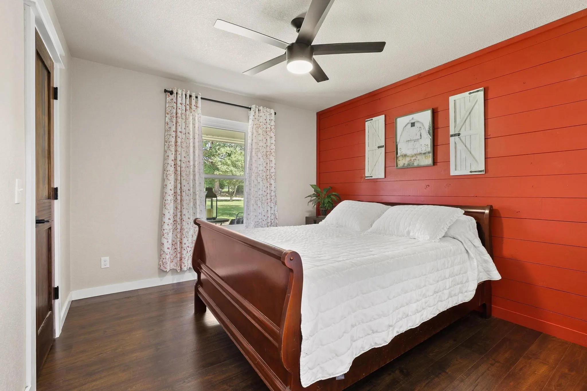 Bedroom featuring a red shiplap accent wall, dark wood-finish flooring, and a ceiling fan with integrated lighting