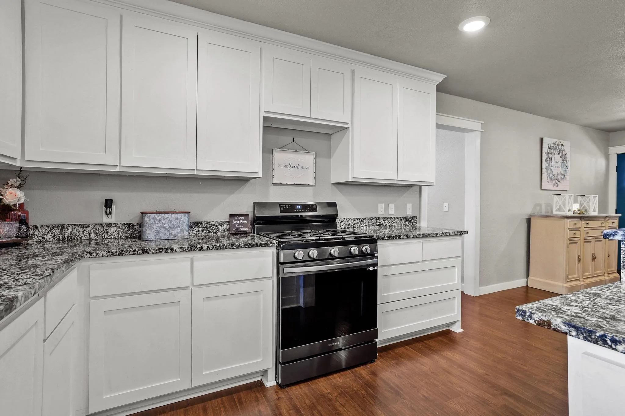 Kitchen featuring white shaker-style cabinetry, dark speckled countertops, a black range, and wood-finish flooring