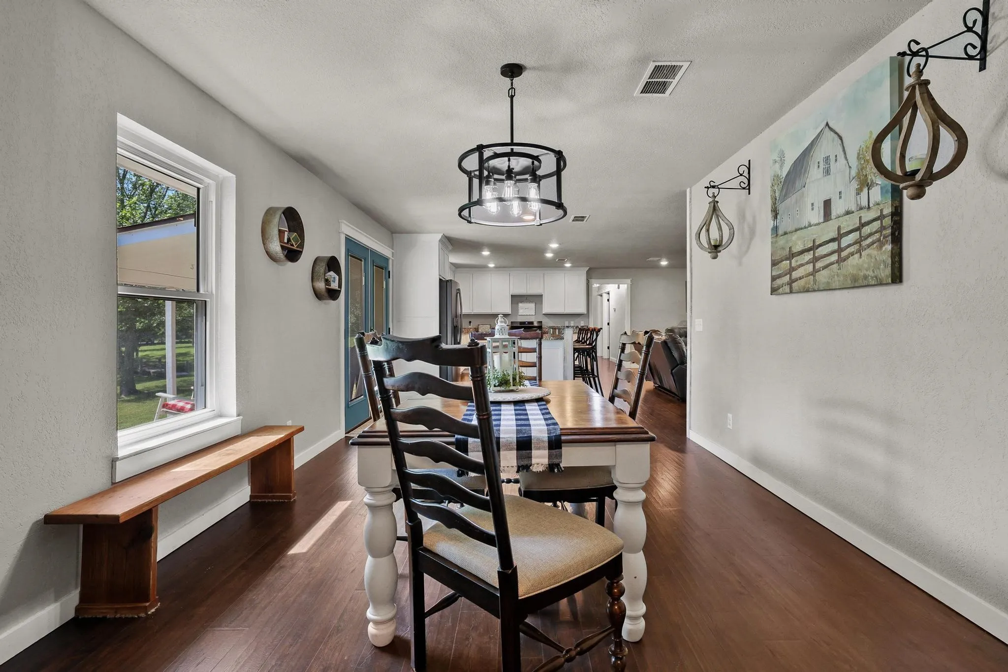 Dining area featuring wood-finish flooring, a contemporary chandelier, light gray walls, and a window providing natural illumination