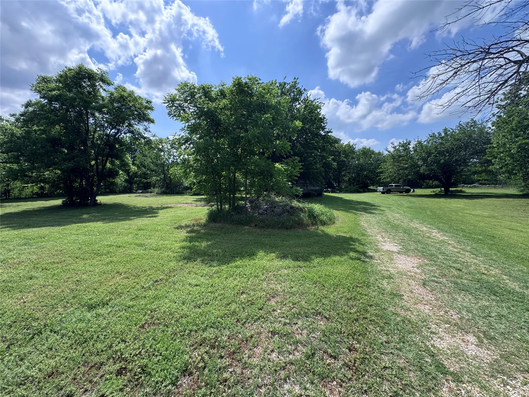 Expansive grassy lot with a gravel path, mature trees, and natural landscaping