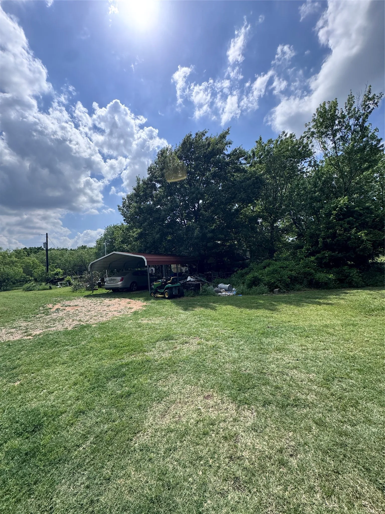 Expansive grassy area featuring mature trees and a detached carport structure