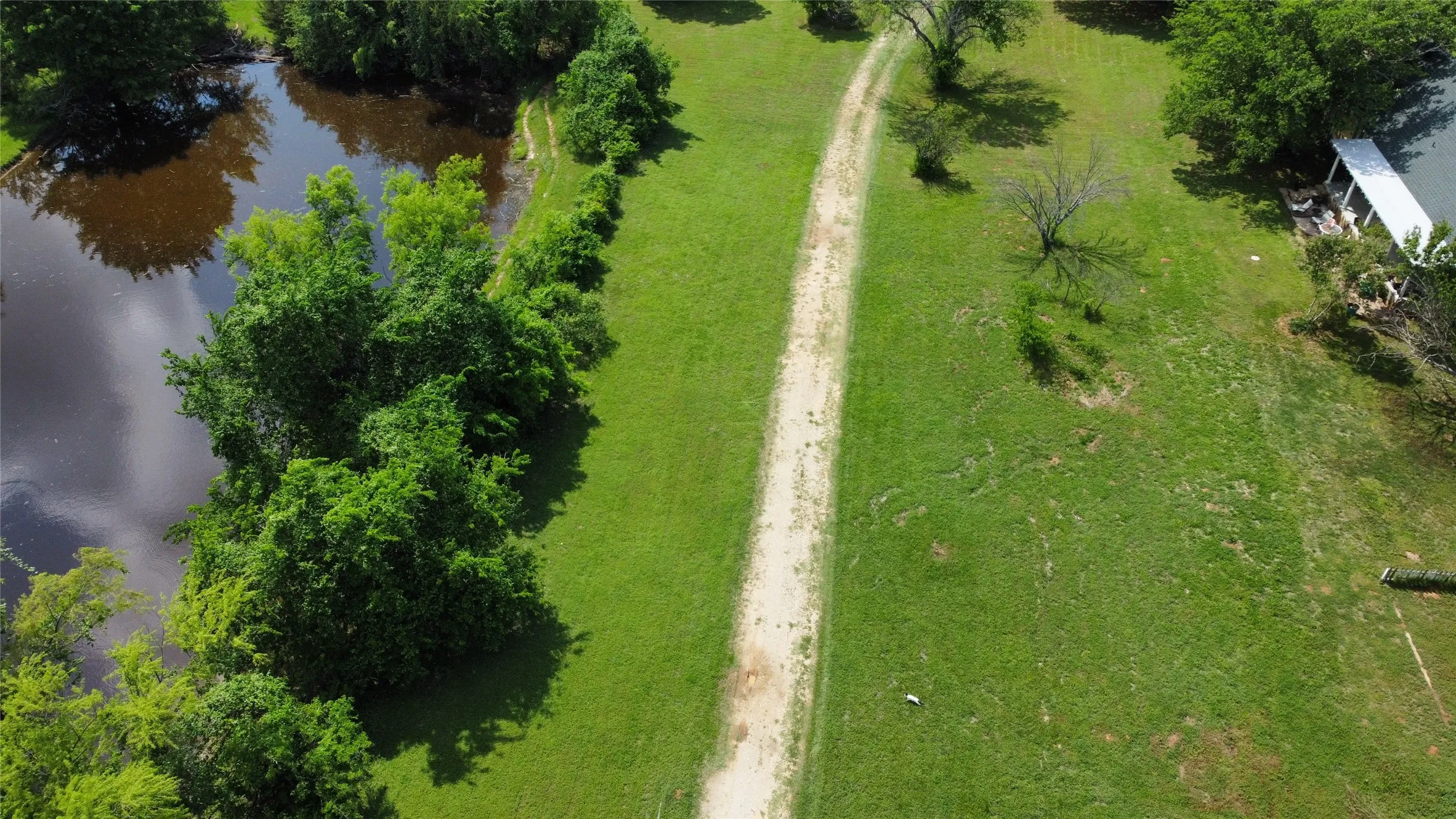 Expansive green grounds featuring a natural pond bordered by lush foliage and a dirt pathway