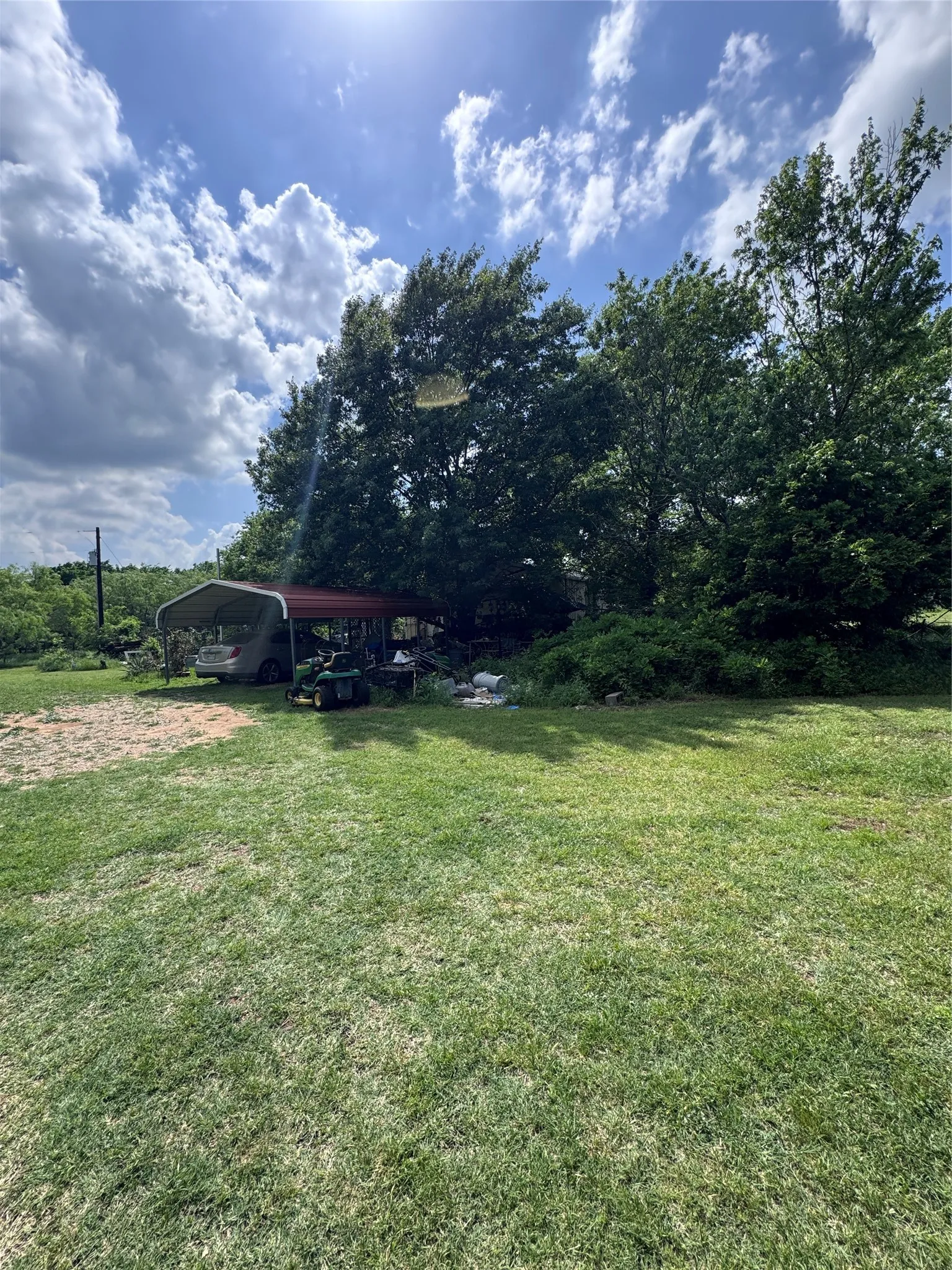 Expansive green lawn with a metal carport featuring a red roof