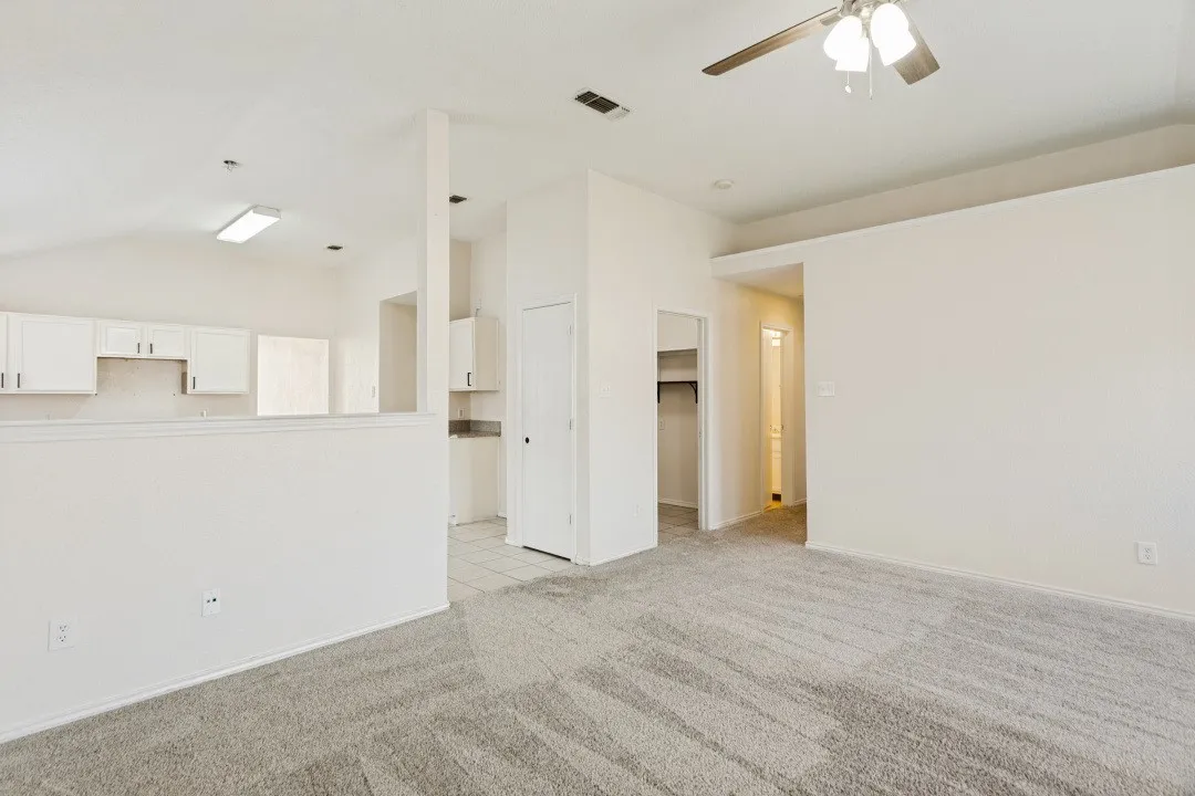 Expansive open concept living area featuring textured carpet flooring and a ceiling fan