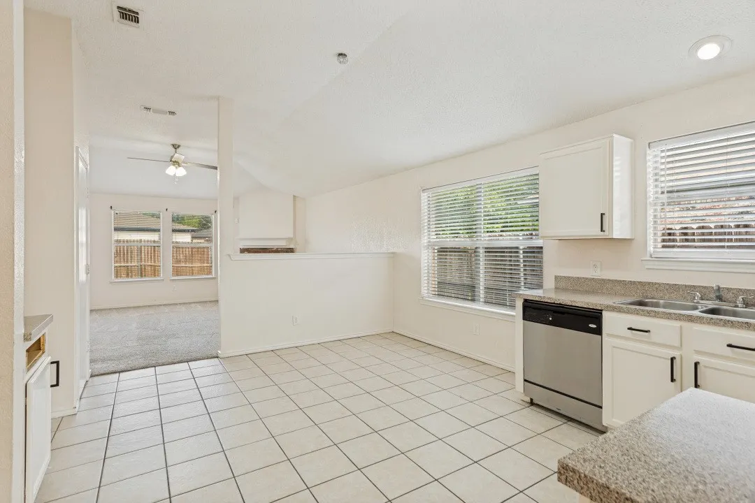 Kitchen featuring white cabinetry, a stainless steel dishwasher, a double basin sink, and granite-look countertops