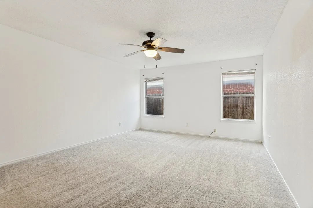 Spacious room featuring light-toned carpeting, two windows, a ceiling fan with integrated lighting, and neutral wall tones