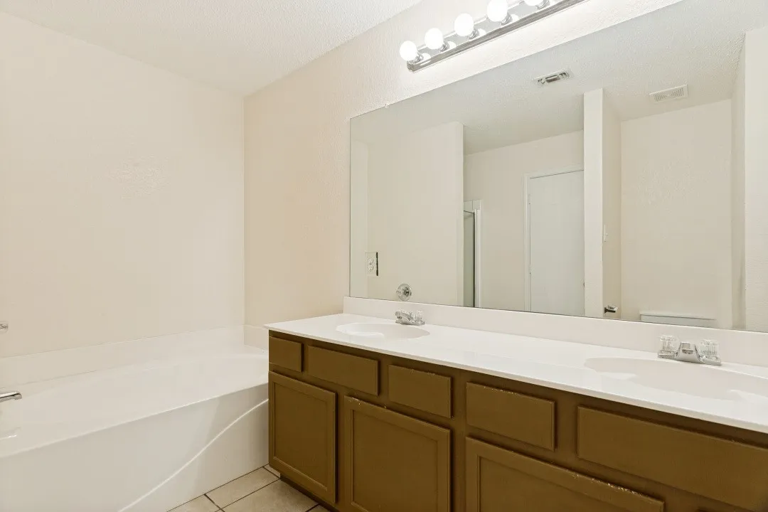 Bathroom featuring a dual vanity with wood-finish cabinetry and a spacious built-in tub