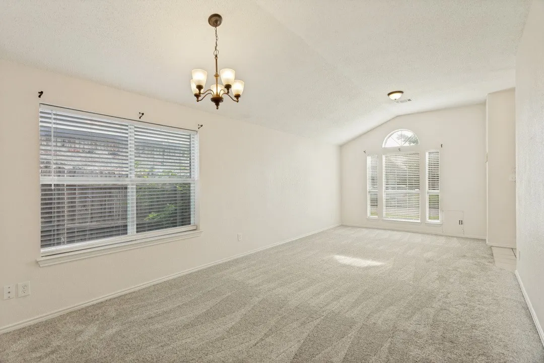 Spacious room featuring vaulted ceilings, a large window with blinds, a multi-pane arched window, and neutral carpet flooring