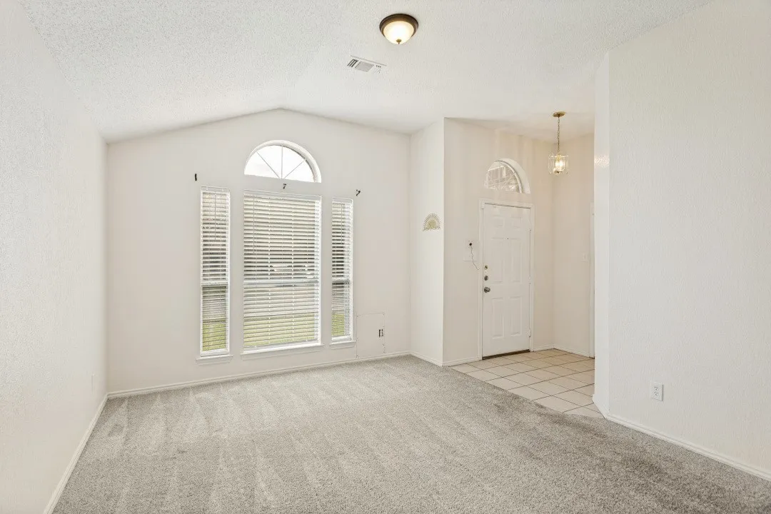 Vaulted ceiling great room with a large arched window and light gray carpet