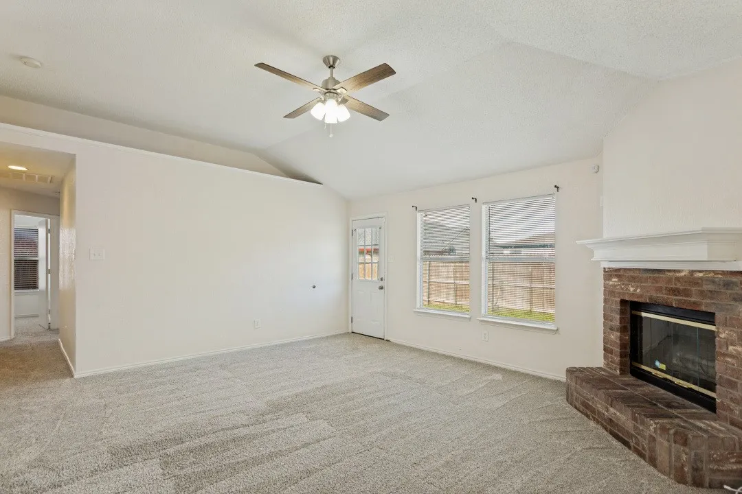 Spacious living area featuring vaulted ceilings, a ceiling fan with integrated lighting, and plush carpeting