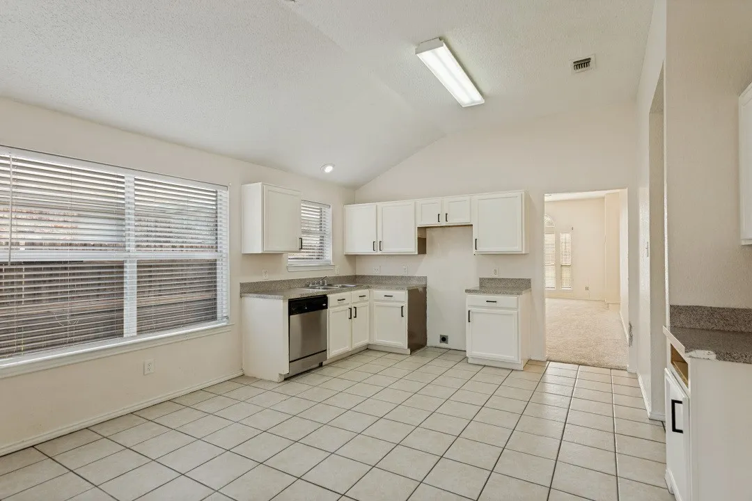 Kitchen featuring white cabinetry, light-toned countertops, a stainless steel dishwasher, and tile flooring