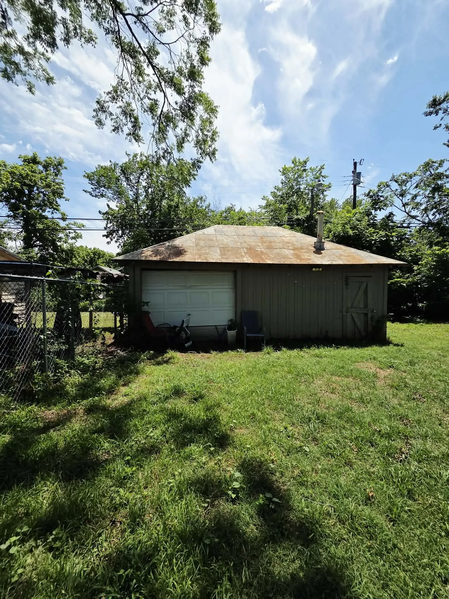 Detached outbuilding featuring a roll-up garage door, a side entrance with a wooden door, and a metal roof