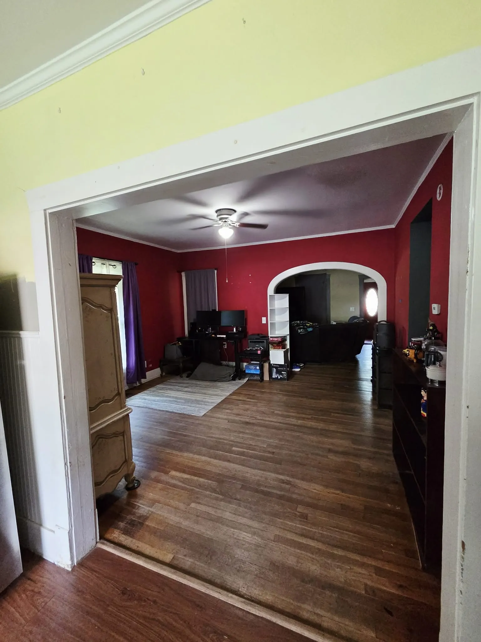 Expansive room featuring wood-finish flooring, a ceiling fan with integrated lighting, and a wide archway to an additional space