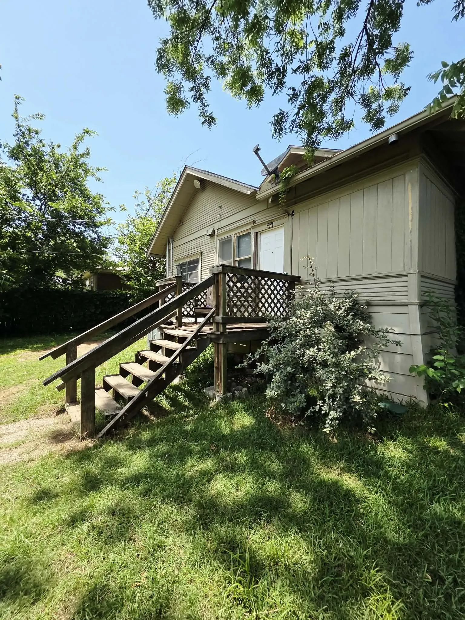 Rear exterior featuring a wood deck with lattice railing, exterior stairs with wood handrails, and a gable roofline