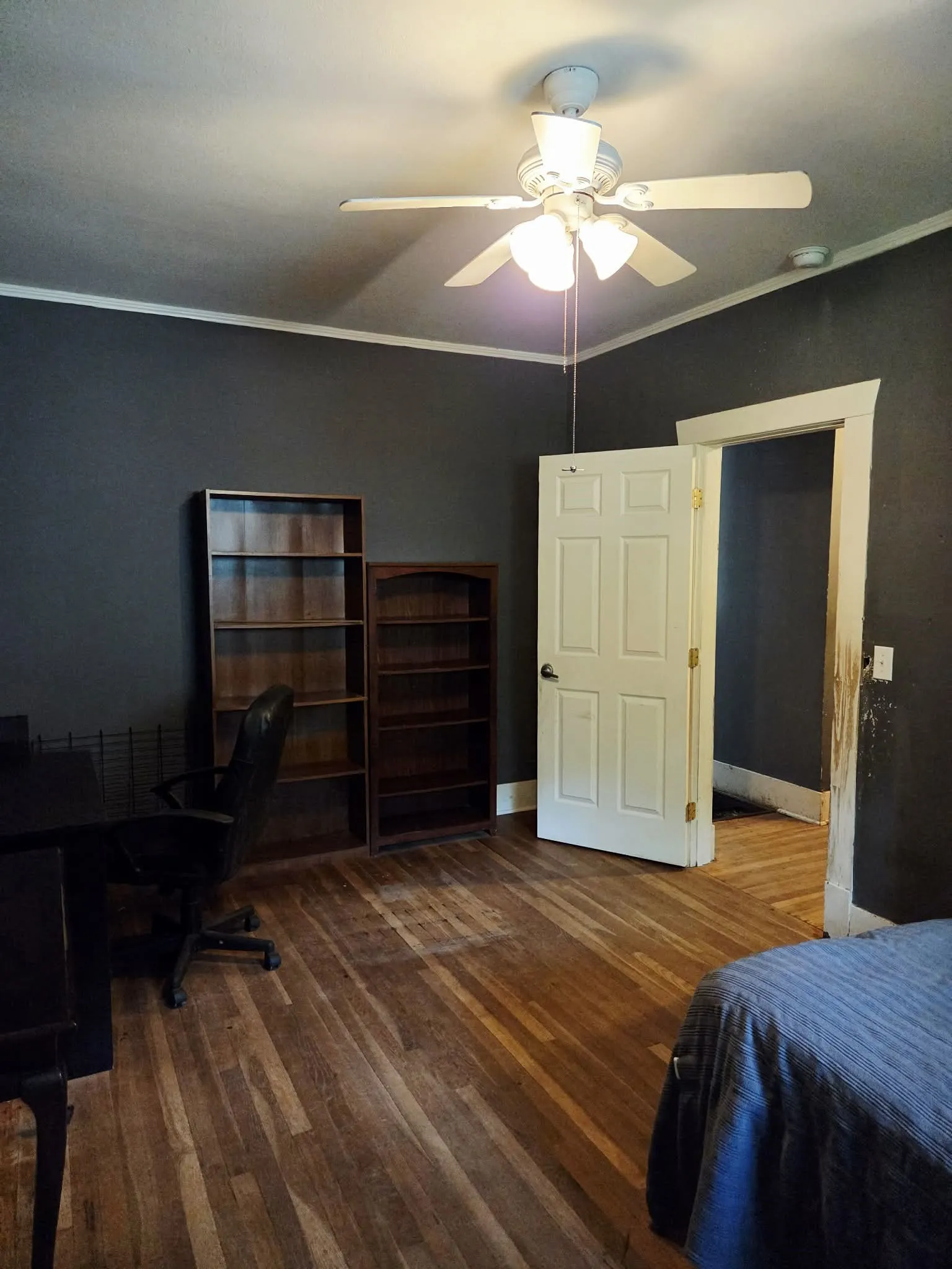 Spacious room featuring wood-finish flooring, a ceiling fan with integrated lighting, and a paneled interior door