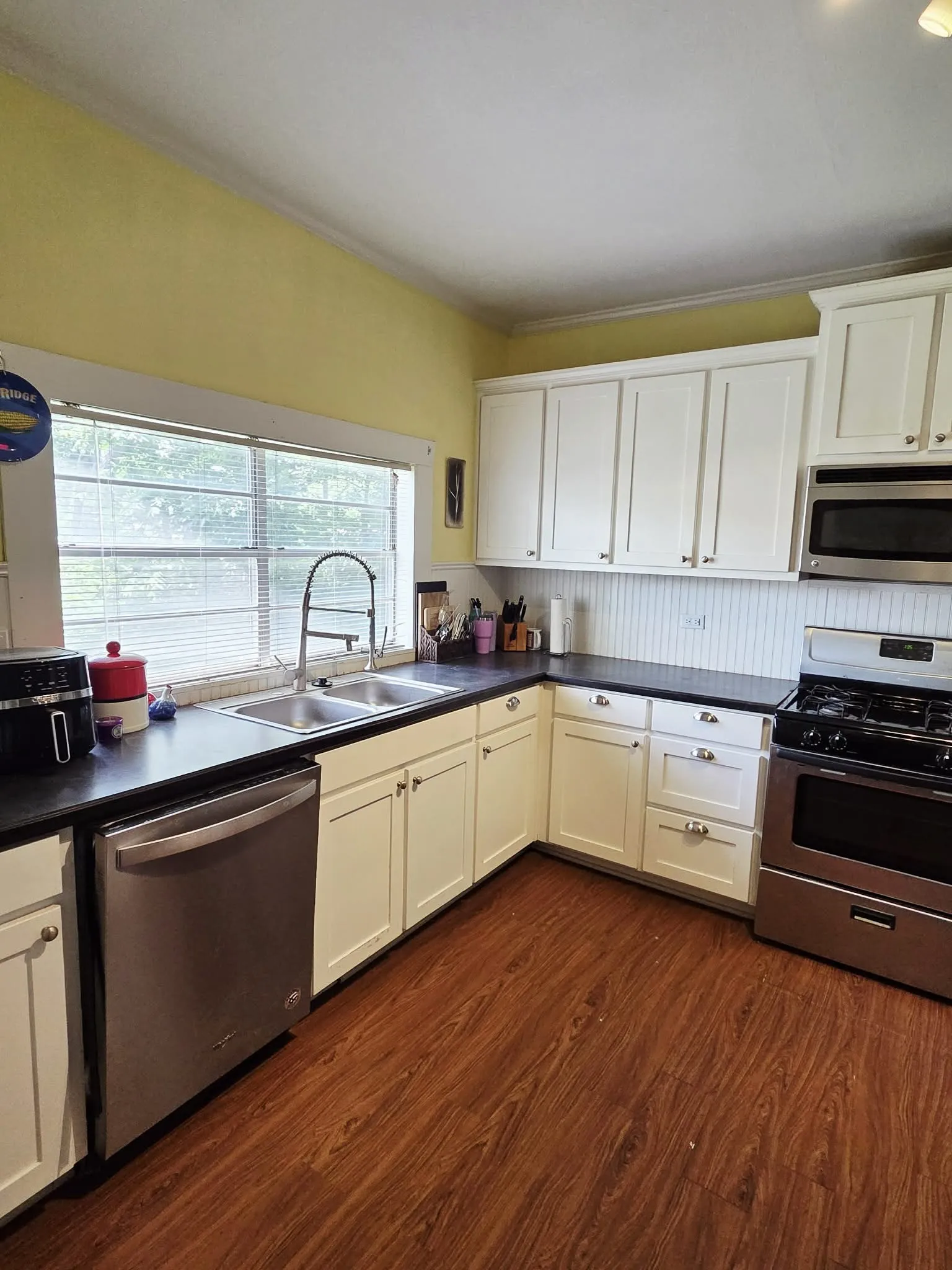 Kitchen featuring white cabinetry, dark countertops, wood-finish flooring, stainless steel appliances, and a double basin sink