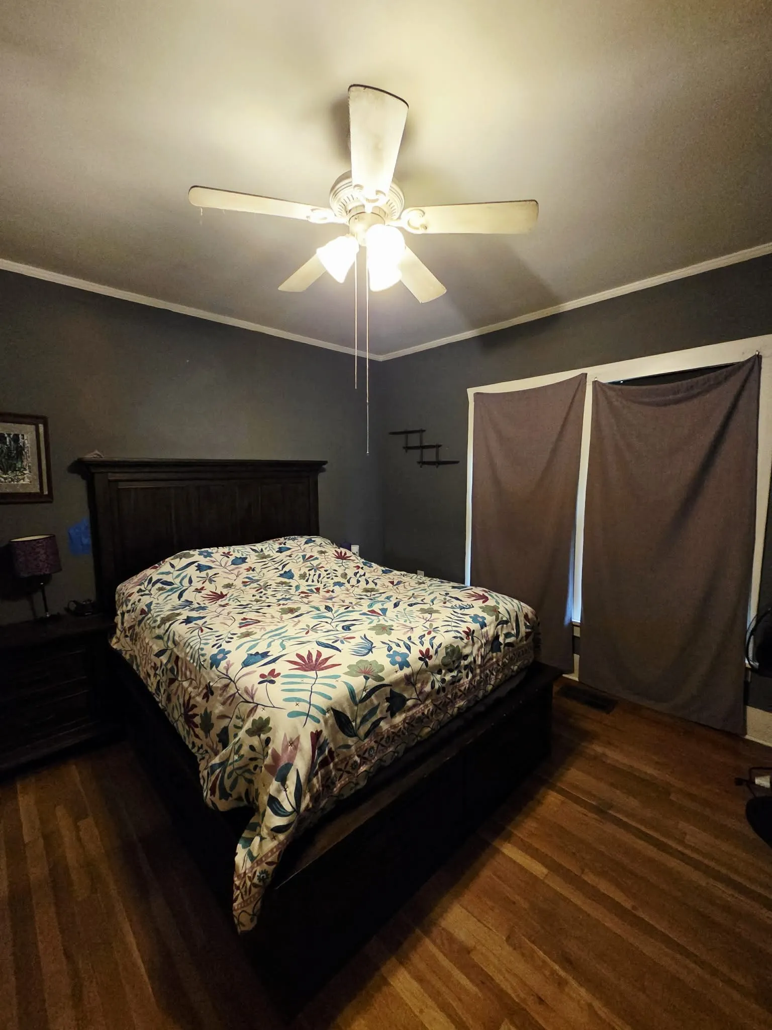 Room featuring wood-finish flooring, a ceiling fan with light kit, and crown molding