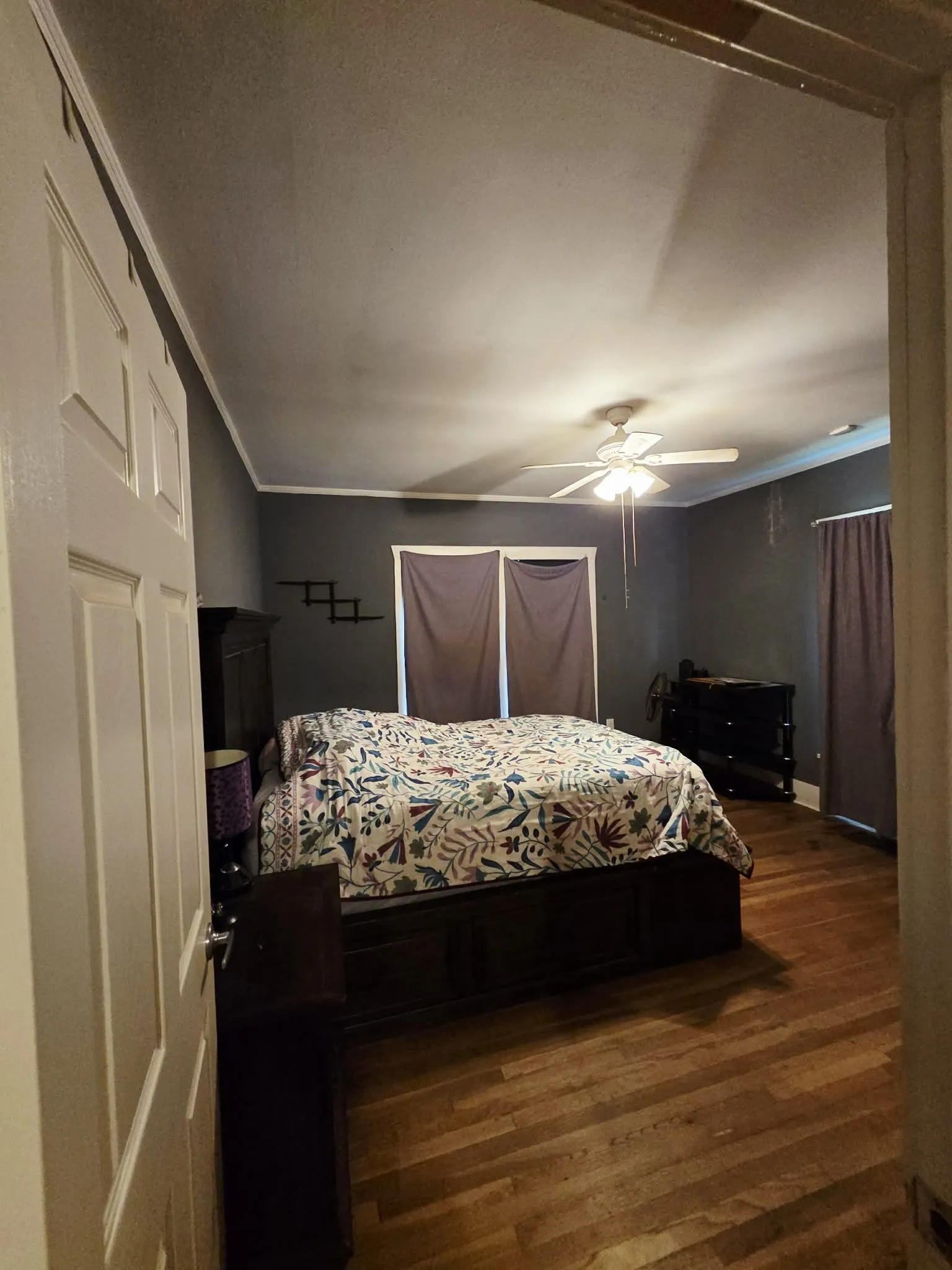 Spacious room featuring wood-finish flooring, a ceiling fan with light fixture, and crown molding